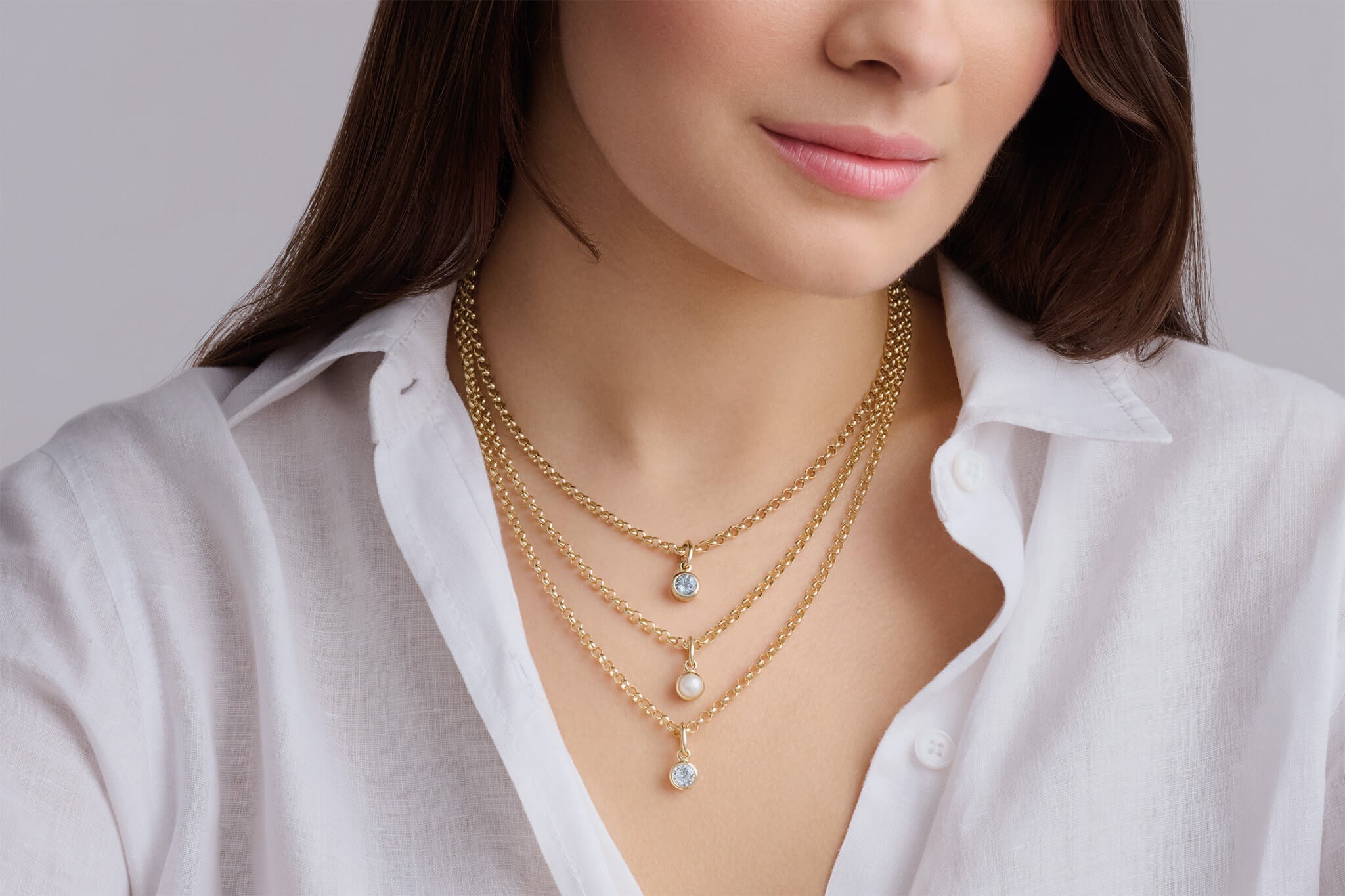 Model wearing three layered necklace chains with small gemstone pendants pearl and blue topaz and aquamarine.