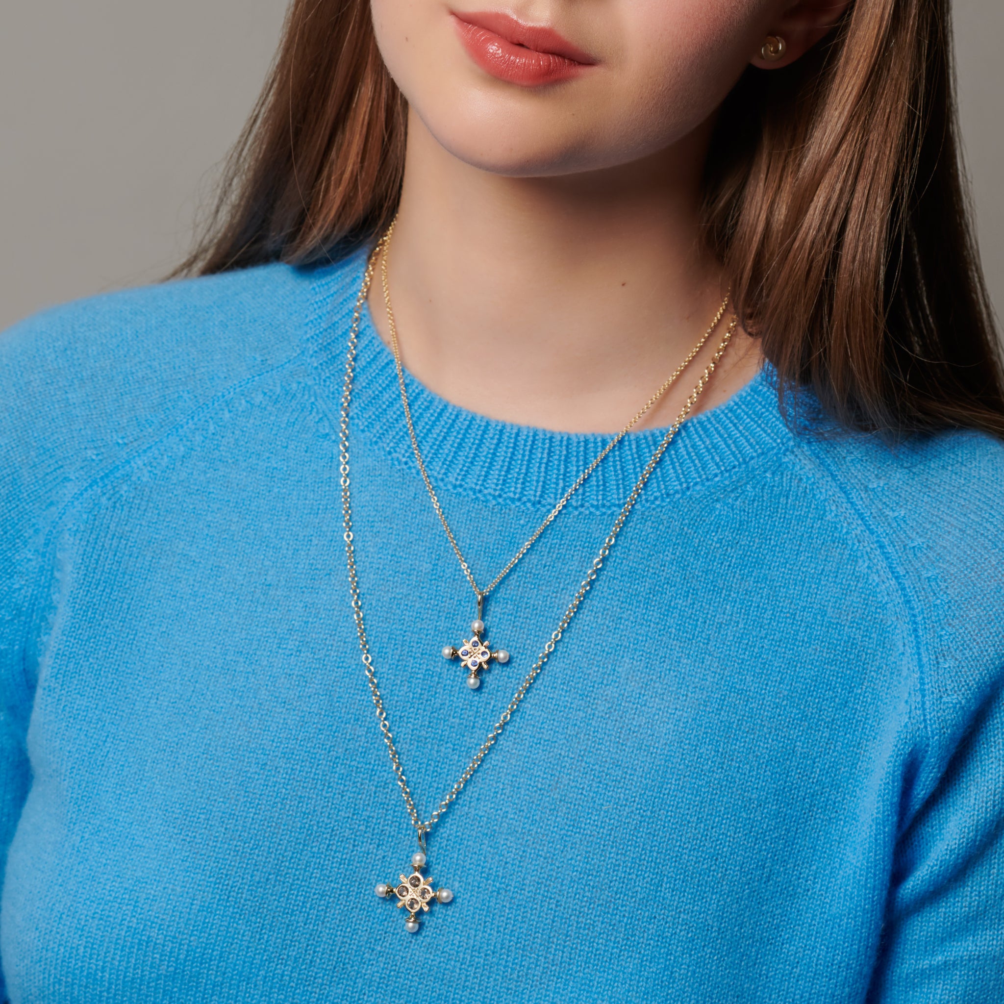 Model wearing two handcrafted cross necklace pendants in precious metals with precious stones.