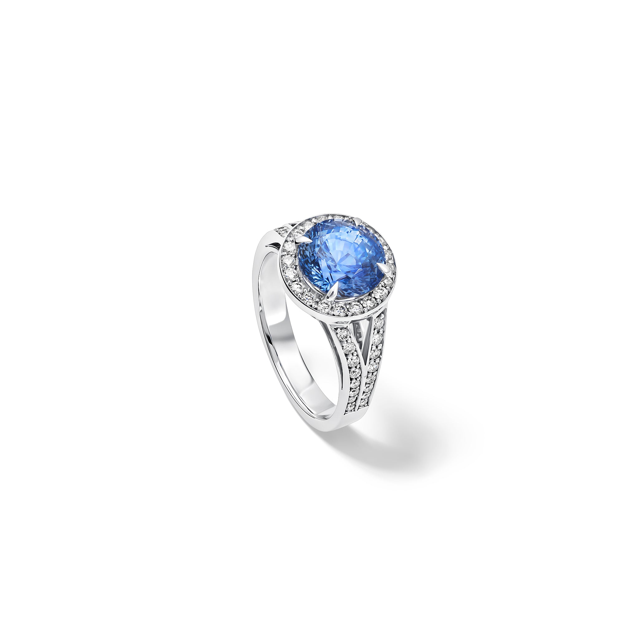 Handcrafted 18ct white gold engagement ring with a large round central blue sapphire surrounded by a halo of small diamonds and smaller diamonds embedded along the band.