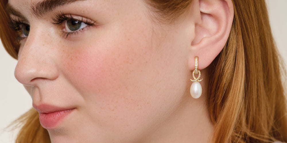 Model looking to the side wearing yellow gold diamond pave Astrea hoops with Icarus drops