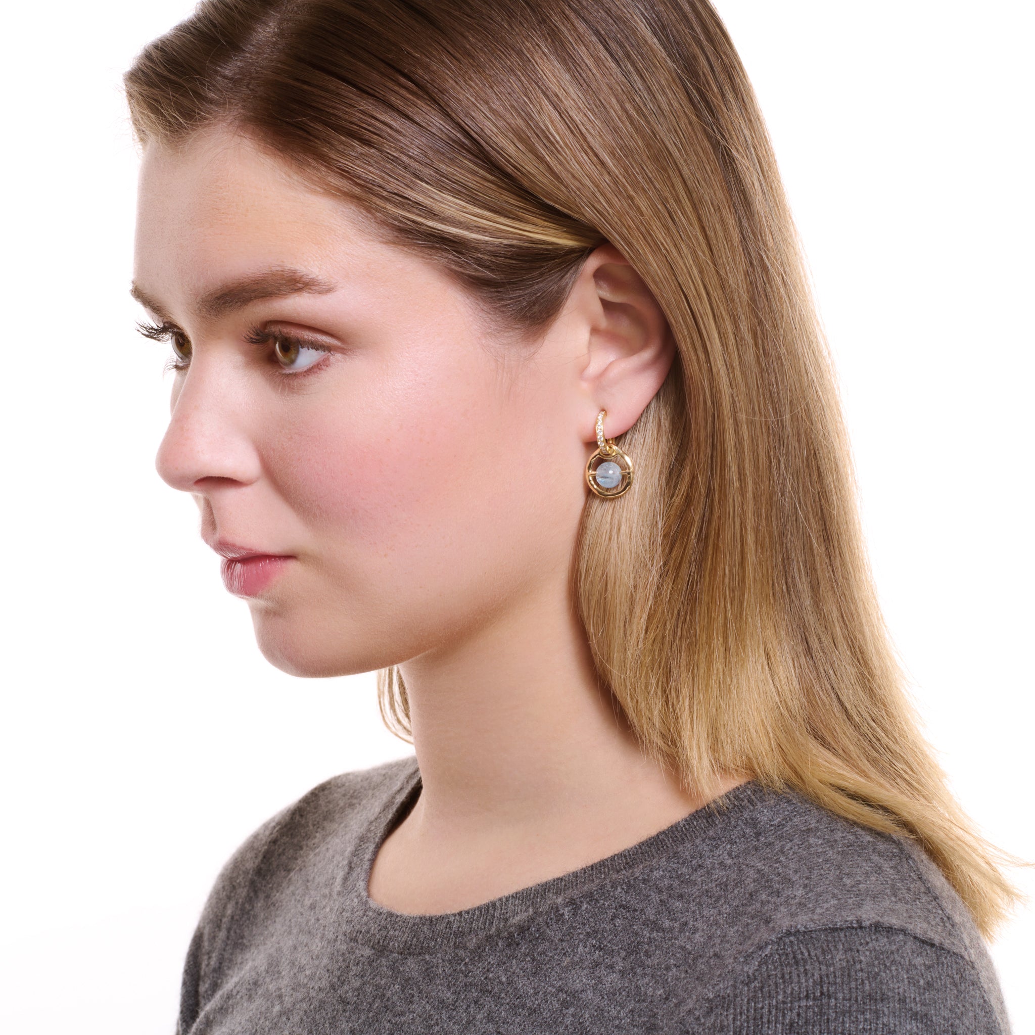 Model wearing handcrafted earring drops in precious metal featuring a round precious stone held within a circle.