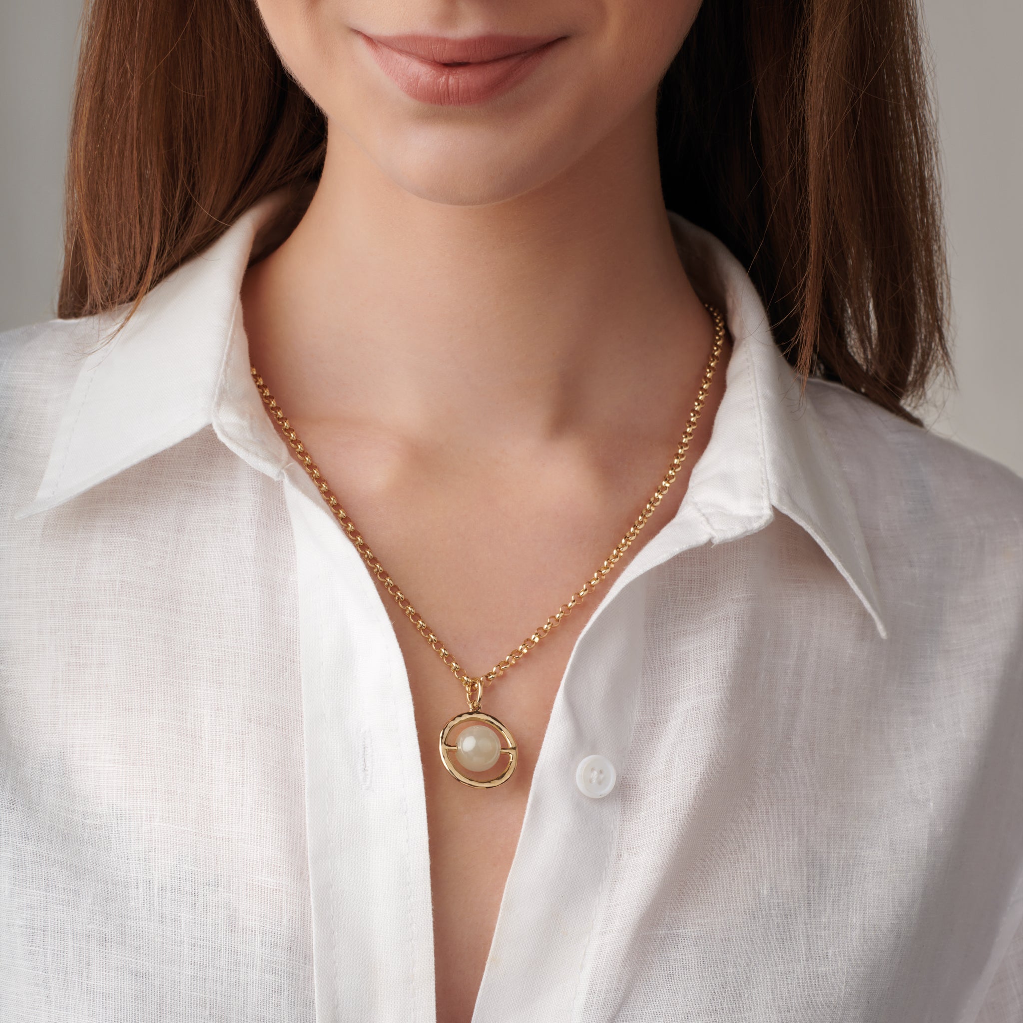 Model wearing a handcrafted necklace pendant in precious metal featuring a circular frame that encircles a precious stone.