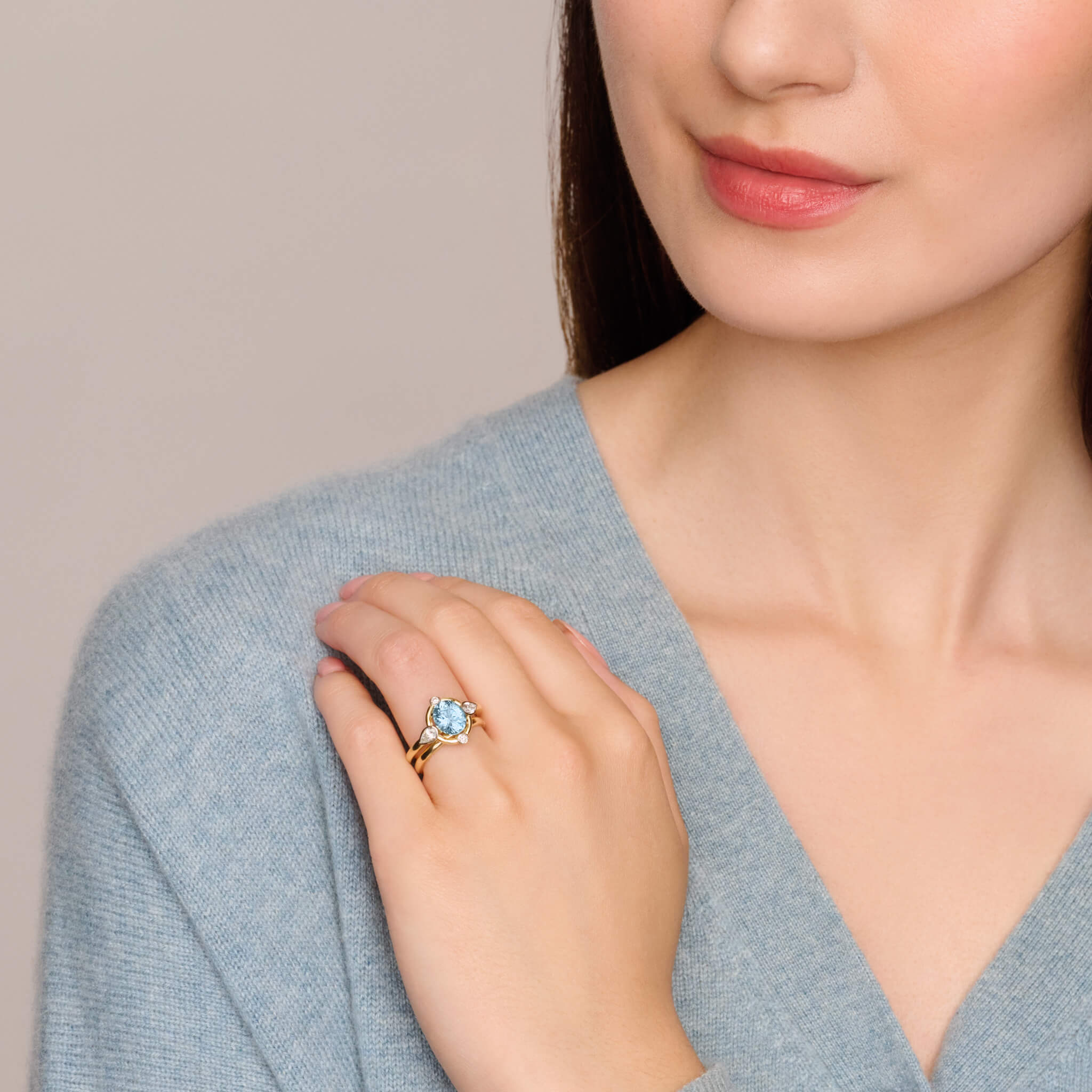 model wears handcrafted 18ct yellow gold engagement ring featuring a soft blue aquamarine at its centre, surrounded by four smaller diamonds, two teardrop-shaped, march birthstone