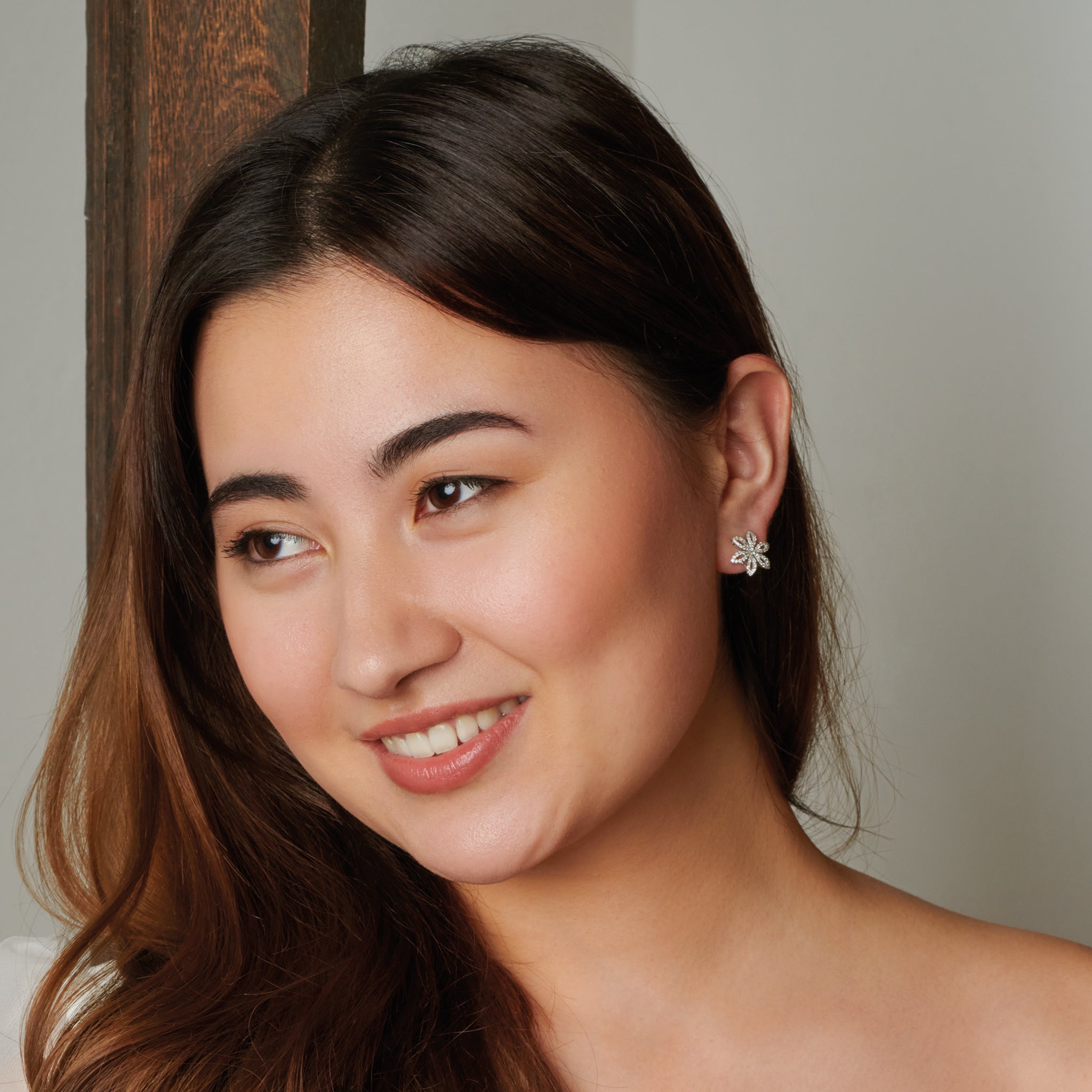 Model wearing handcrafted precious metal flower studs with precious gemstones.