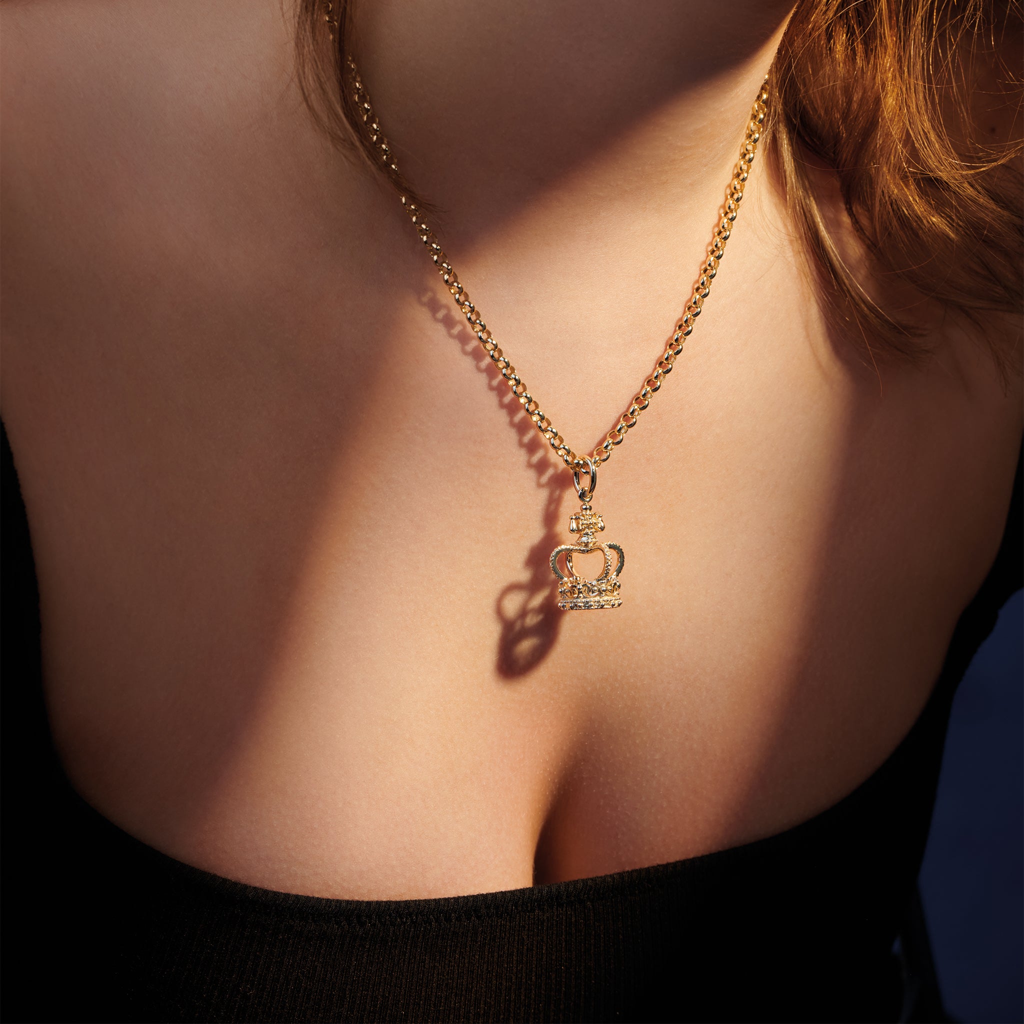 Model wearing handcrafted precious metal charm pendant inspired by the crown worn by King Charles III at his coronation.
