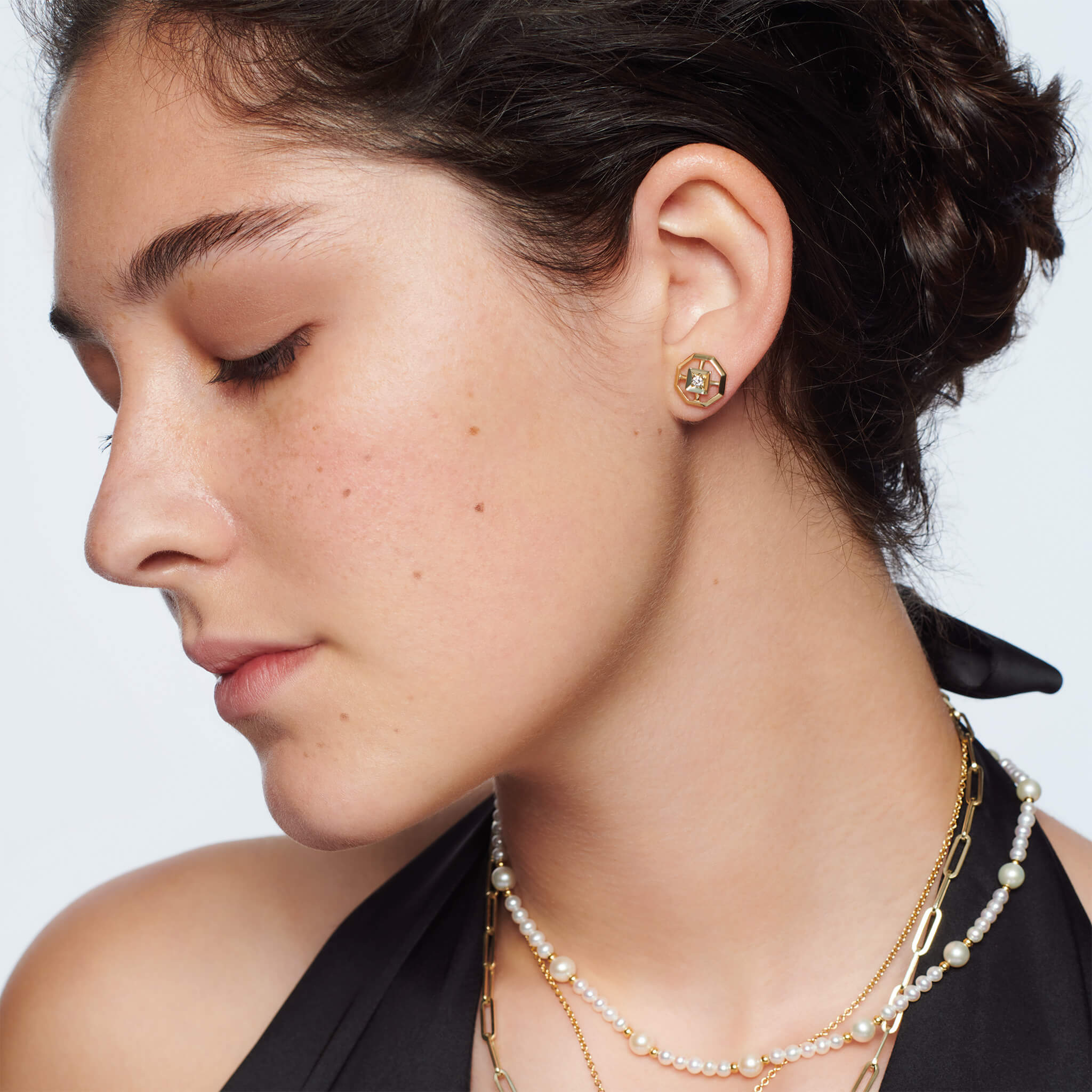 Model wears handcrafted yellow gold stud earrings featuring an octagonal design with a central diamond, birthstone of April.