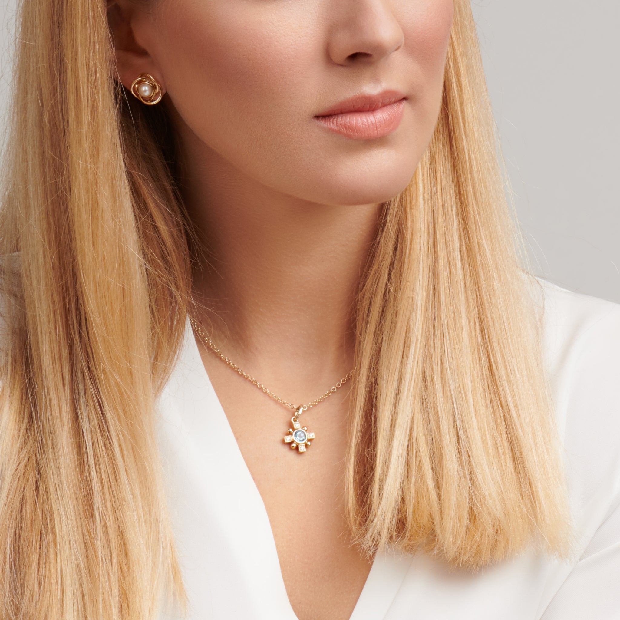 Model wearing a handcrafted Quadro cross necklace pendant in precious metal featuring a central precious stone.