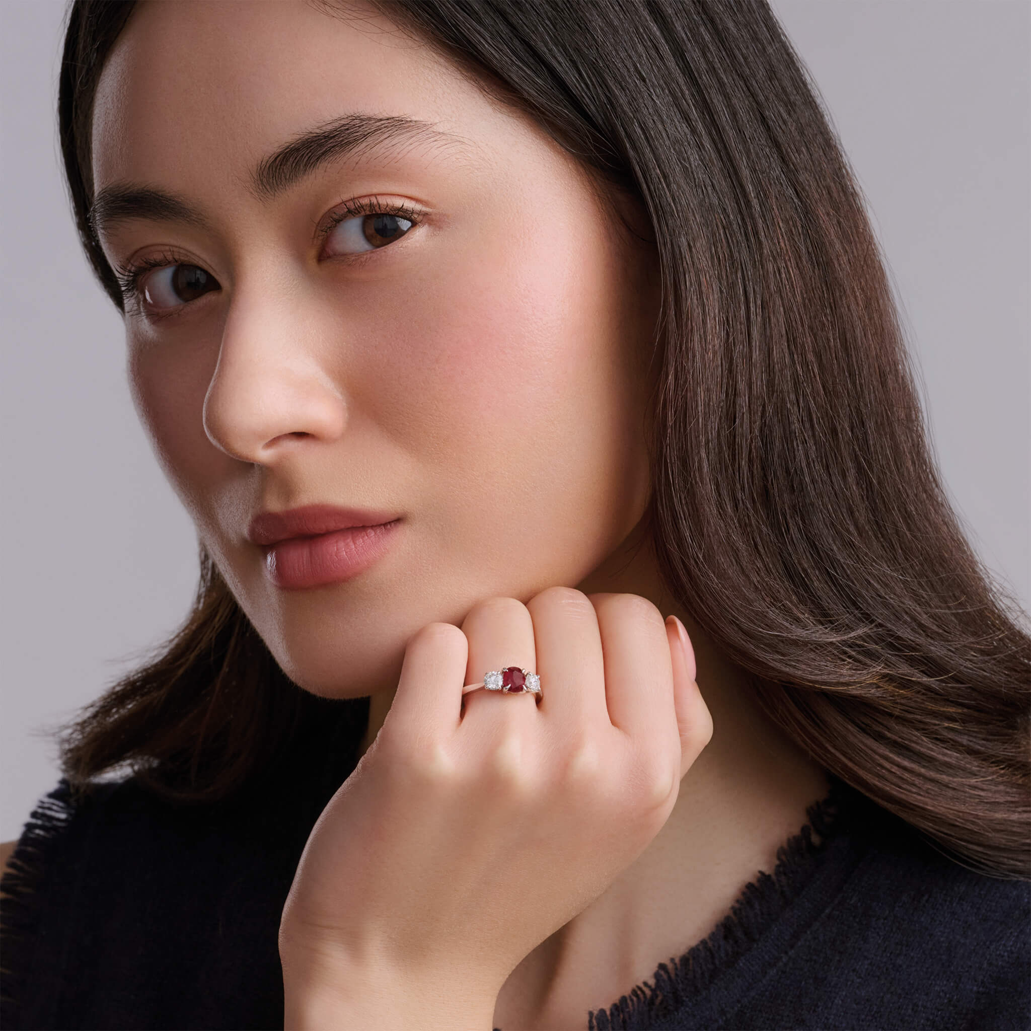 Model wearing a handcrafted 18ct white gold engagement ring featuring a large, oval ruby at its centre, surrounded by two smaller teardrop-shaped white diamonds.