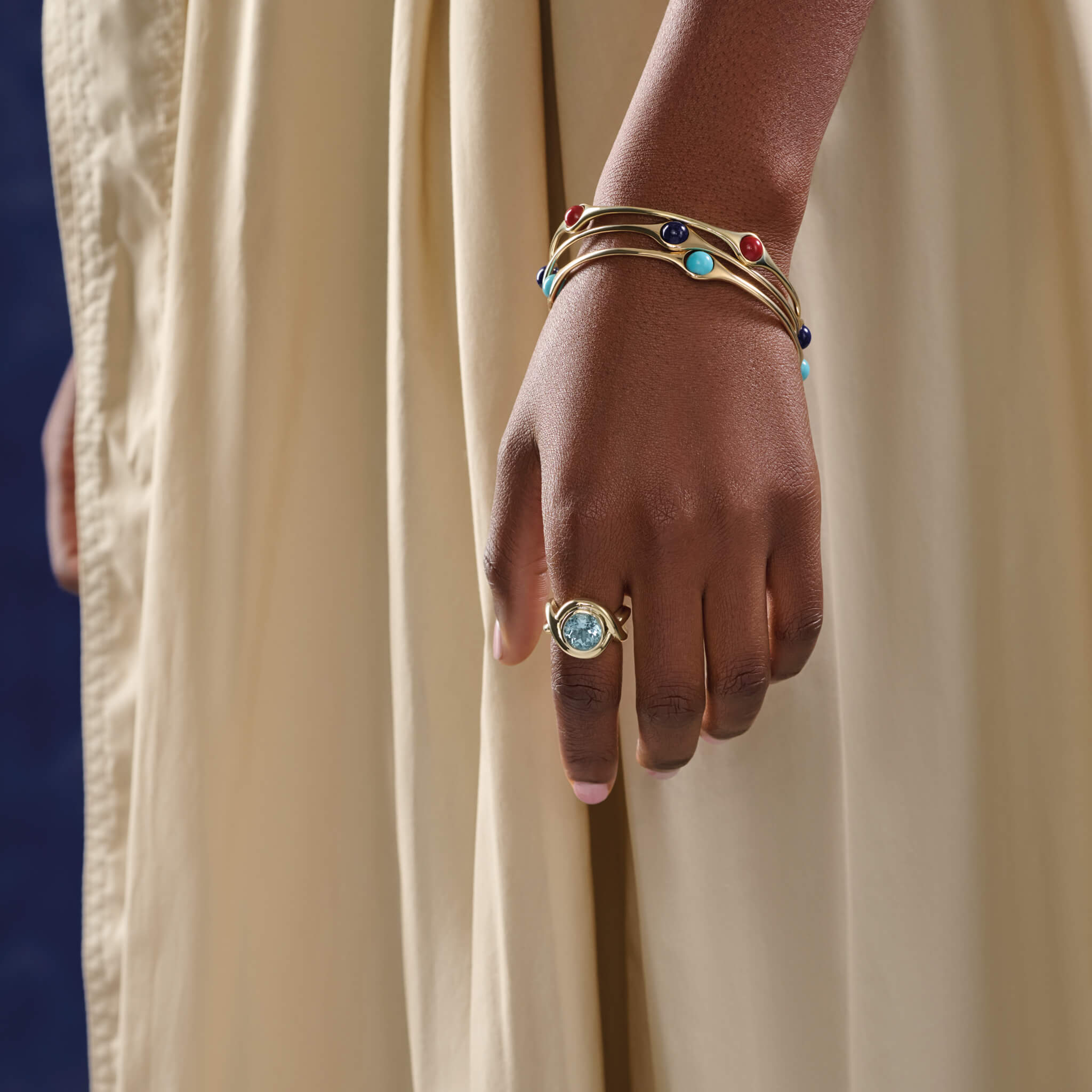 Model wearing handcrafted yellow gold ring featuring curved shanks with a round blue topaz, birthstone of November.