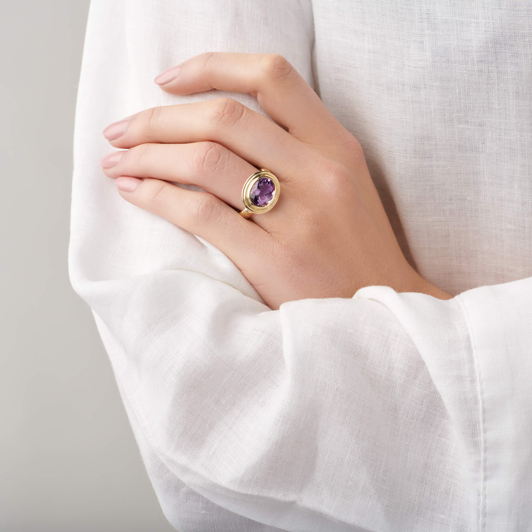 model wears handcrafted yellow gold ring featuring a prominent oval amethyst, birthstone of February.