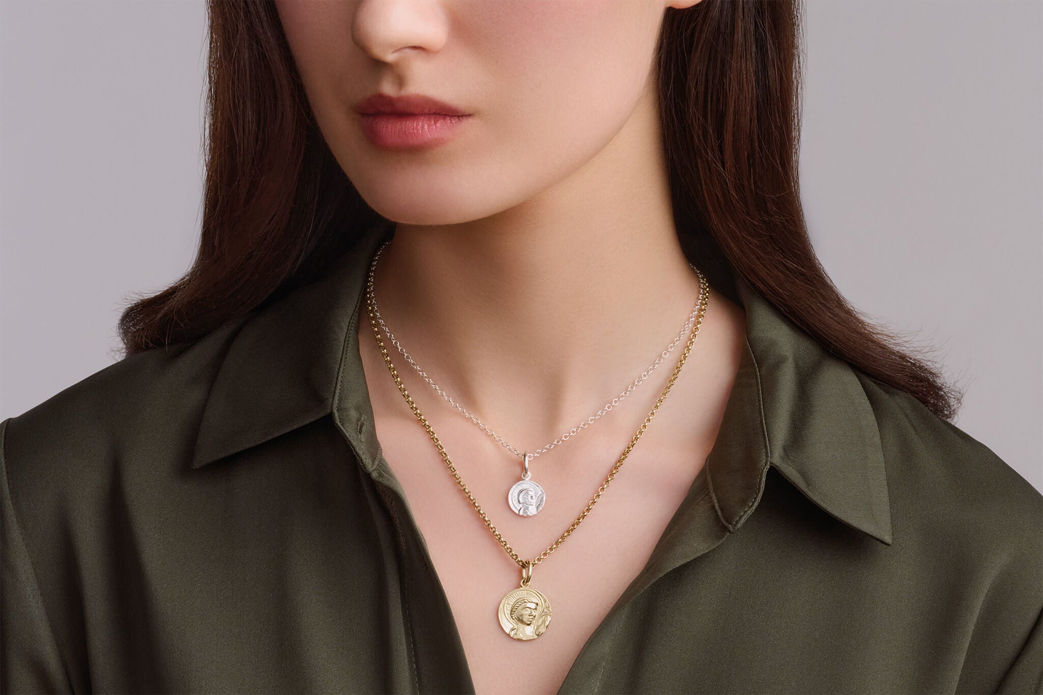 Model wearing handcrafted saint pendants in yellow gold and silver for a mixed metal look.