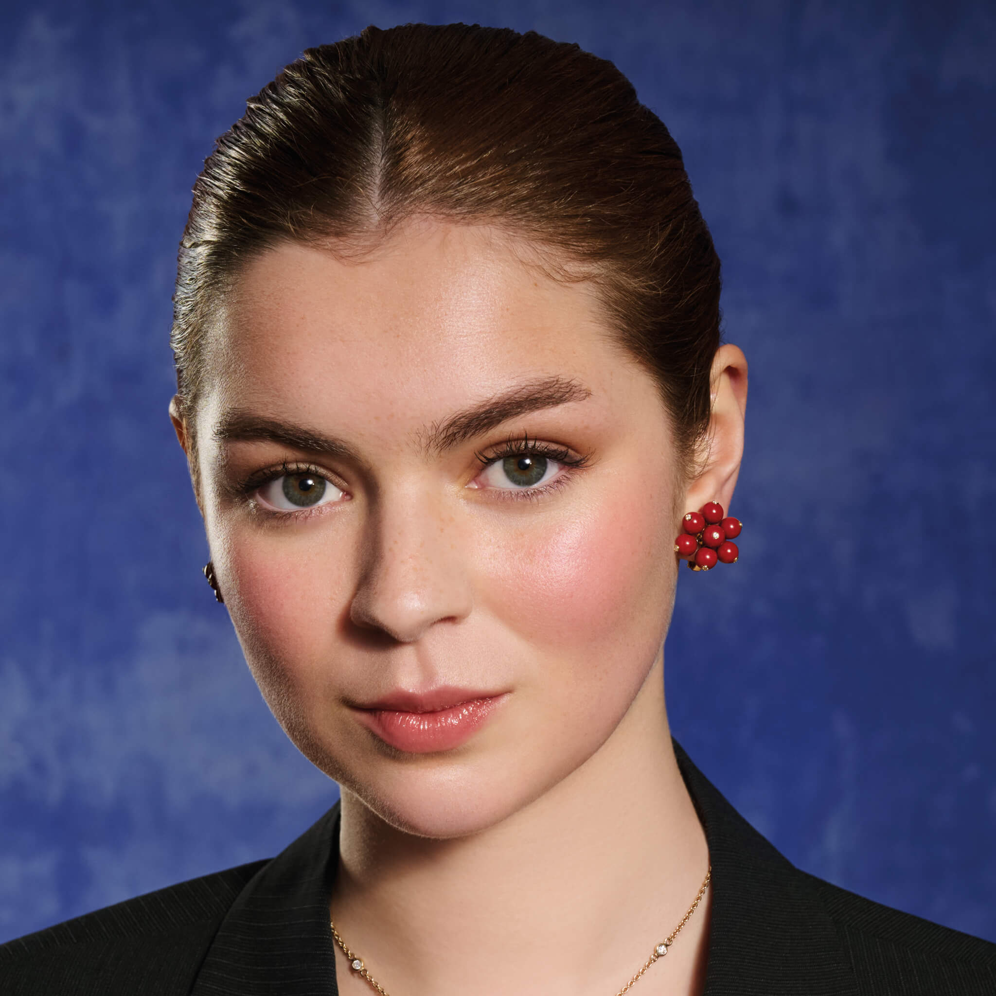 Model wears handcrafted 18ct yellow gold earrings featuring a cluster of red coral beads, interspersed with small diamonds.
