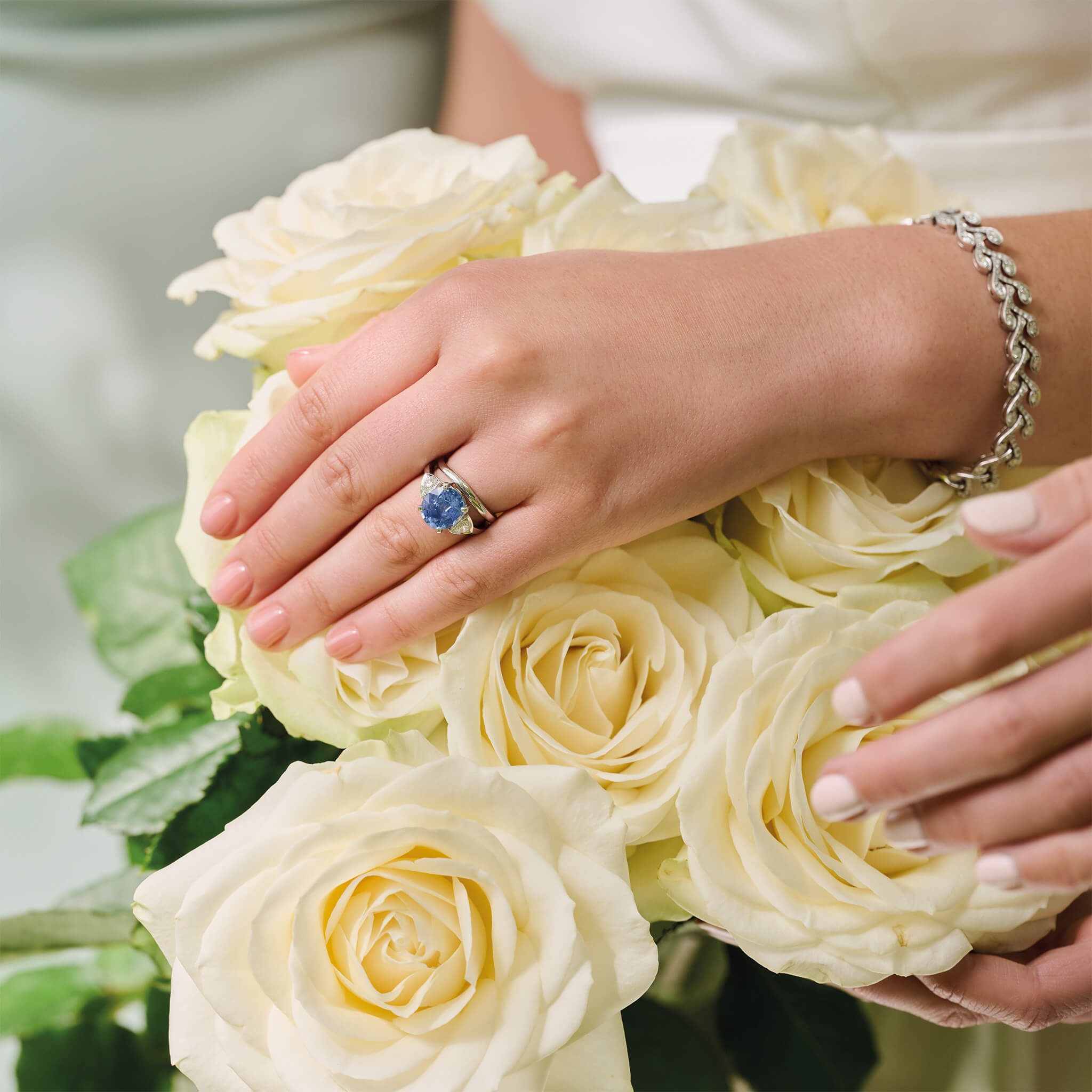 Model wearing a handcrafted 18ct precious metal engagement ring featuring a large central oval sapphire flanked by one smaller teardrop-shaped diamond on each side.
