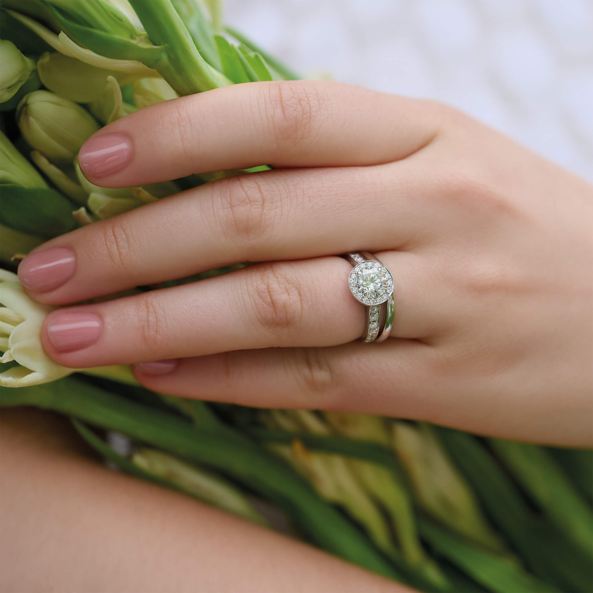 Model wears handcrafted platinum engagement ring with a round diamond at the centre, surrounded by diamond pave.