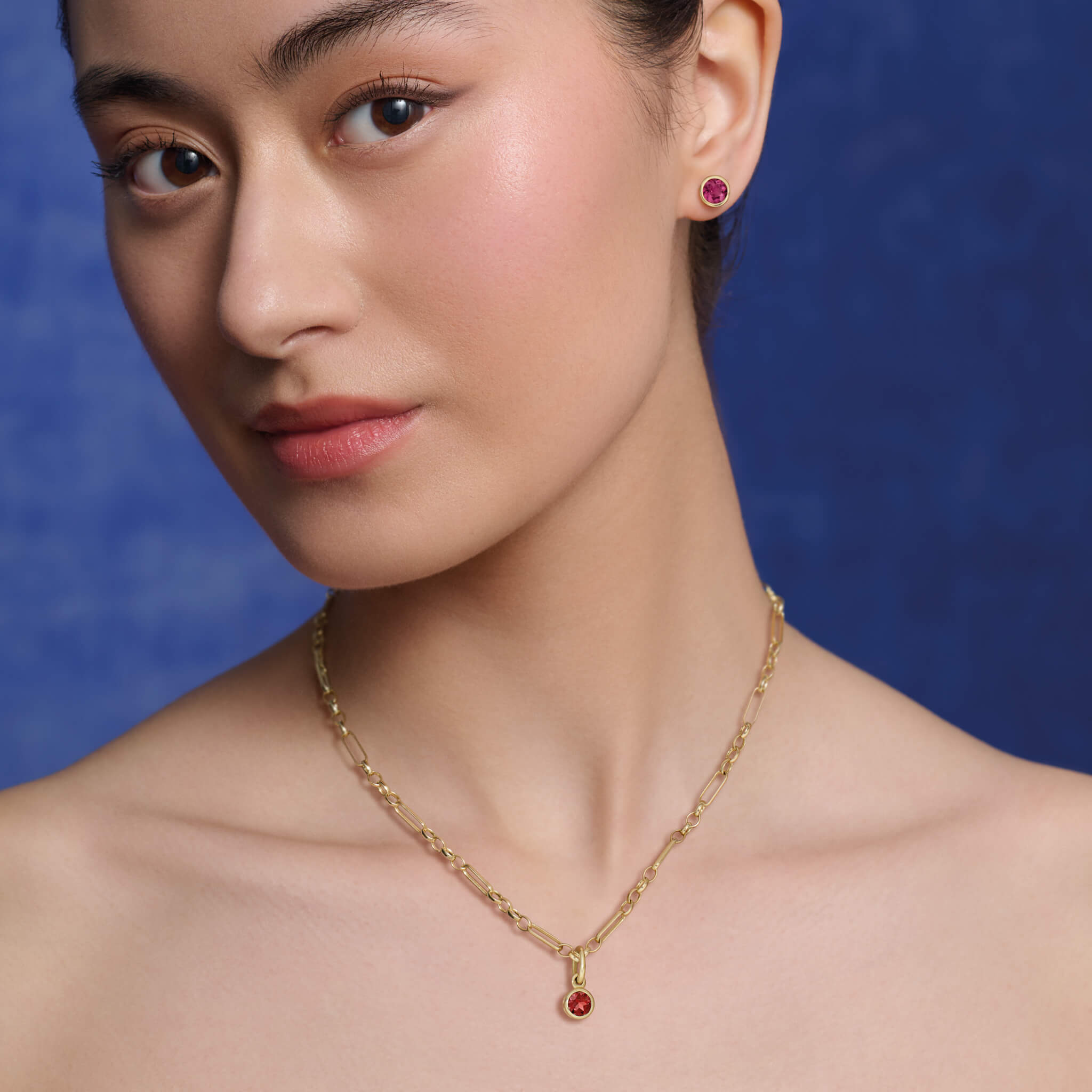 model wears handcrafted necklace pendant in yellow gold featuring a round garnet drop, birthstone of January.