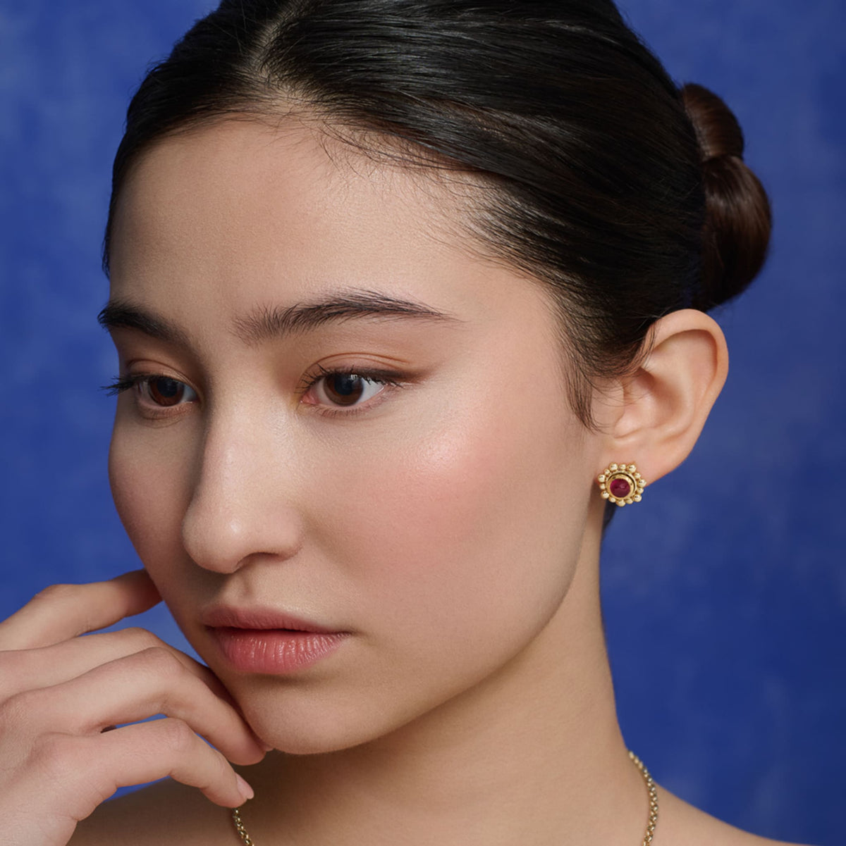 Model wears handcrafted Theresa stud earrings in 9ct yellow gold with cabochon ruby, birthstone for July