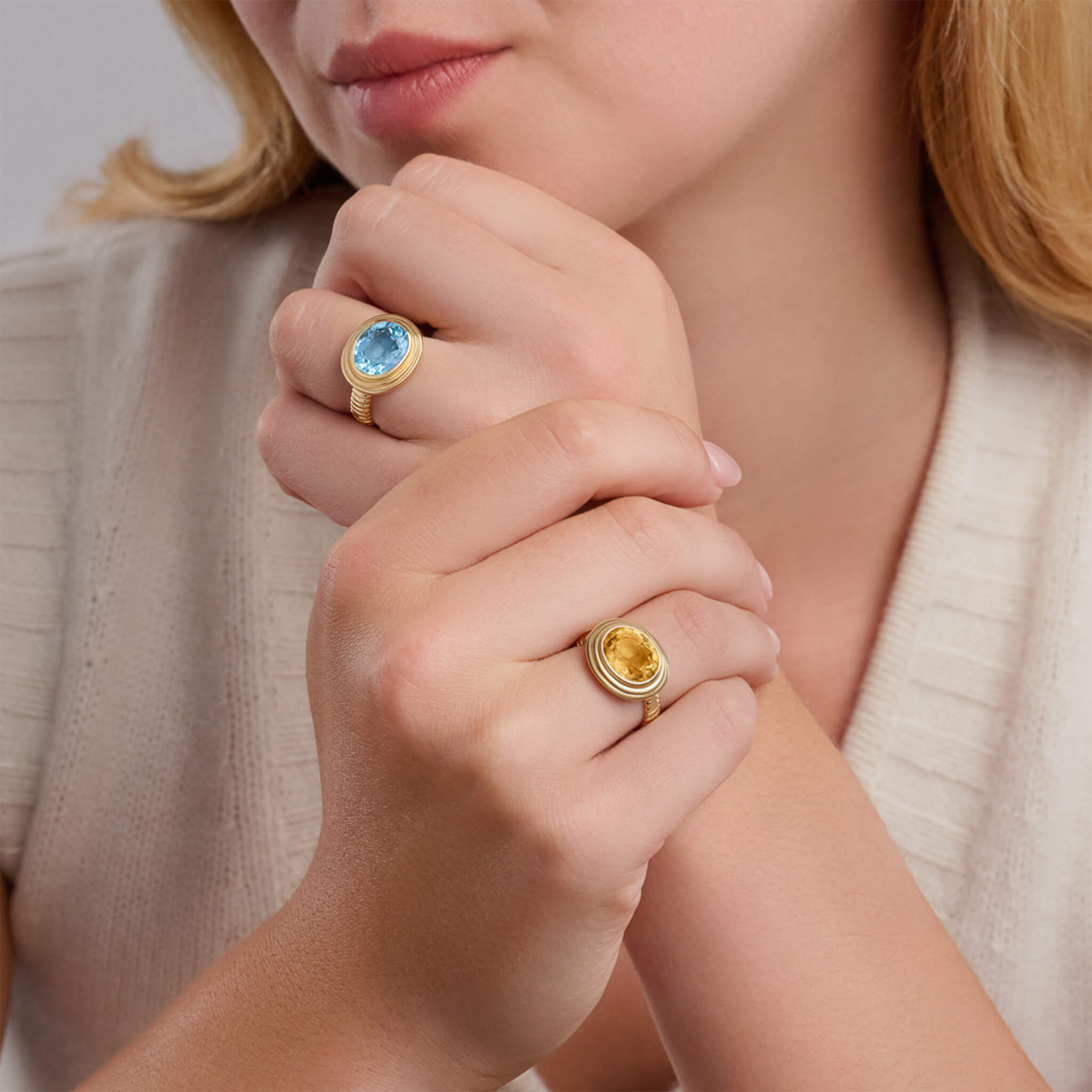 model wears handcrafted yellow gold ring featuring an oval citrine and blue topaz, birthstone of November