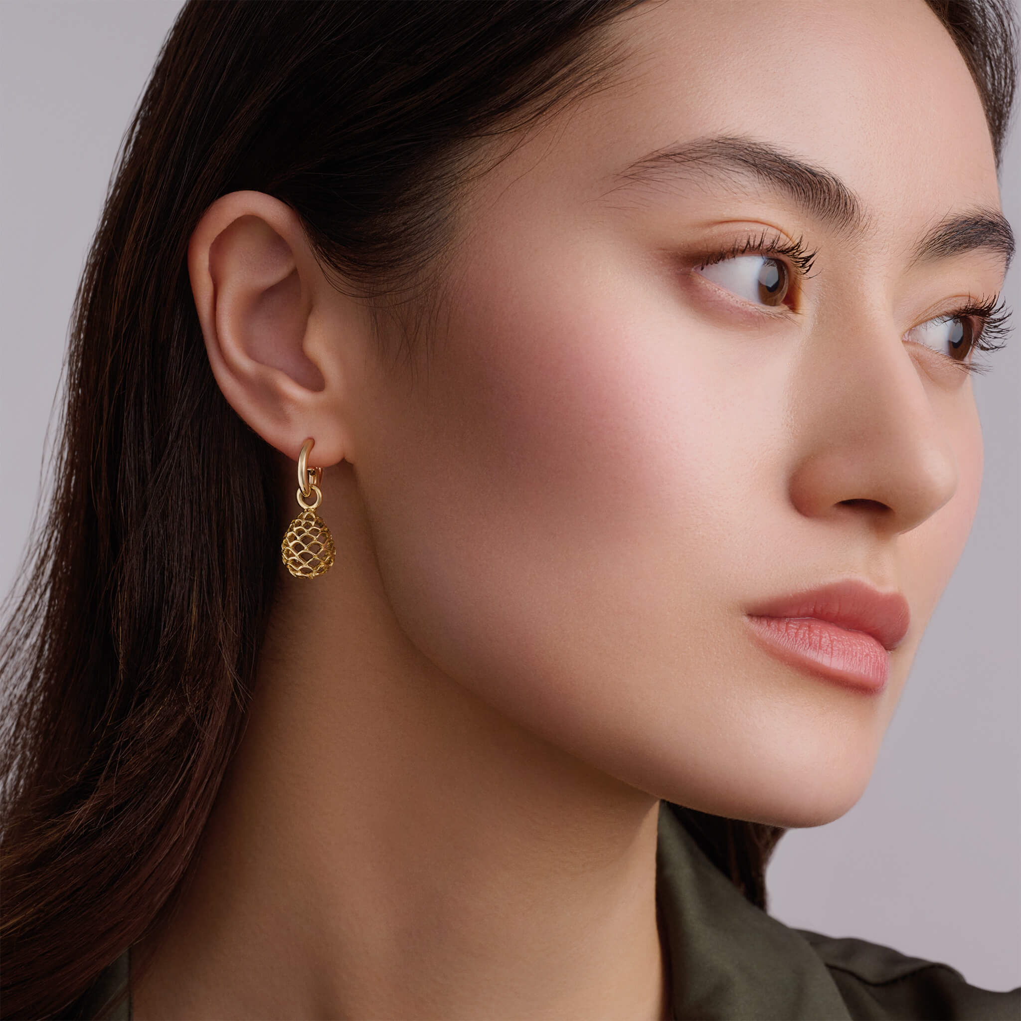 Model wearing handcrafted yellow gold earring drops featuring a pinecone frame.