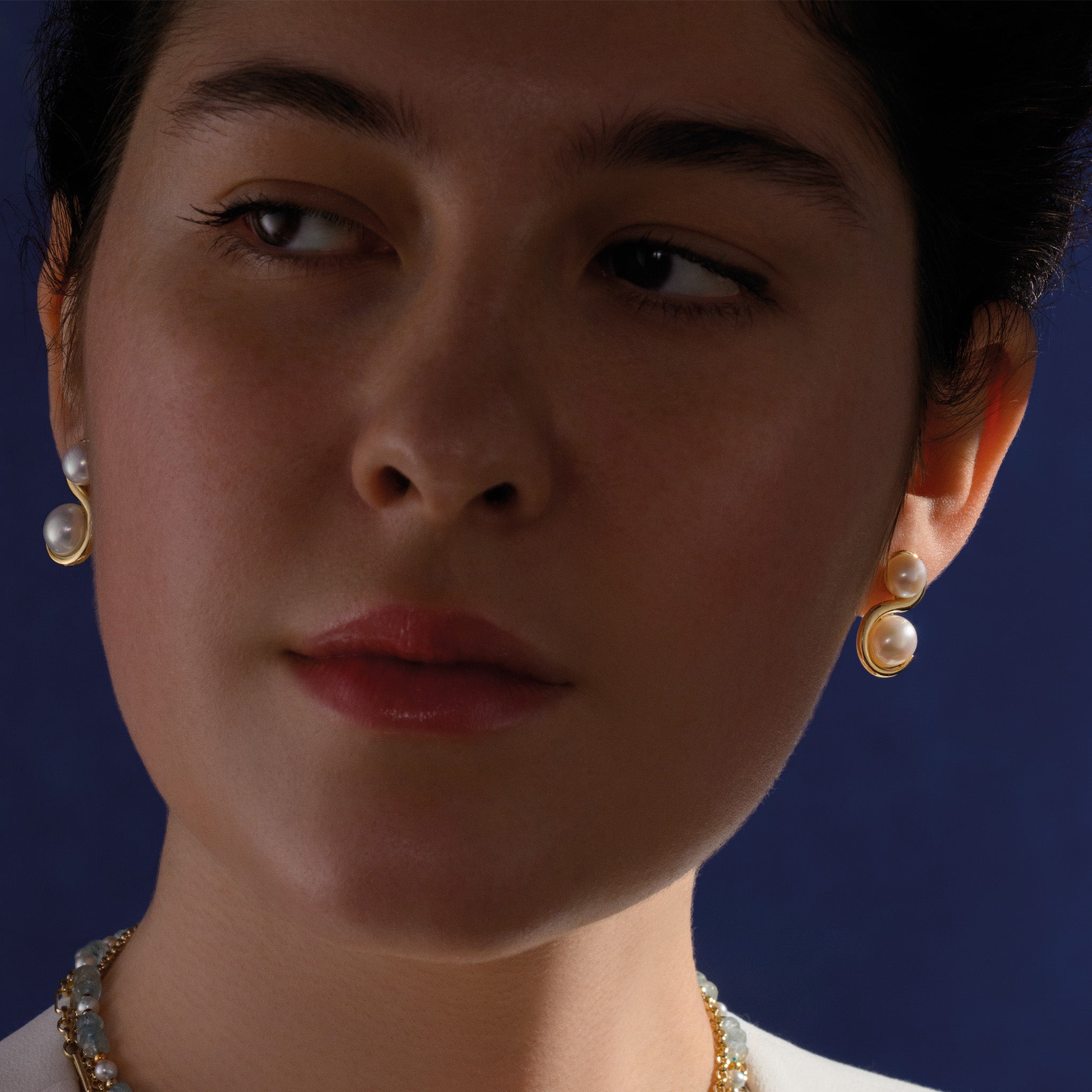 Model wearing handcrafted 18ct yellow gold earrings featuring an 's' shape linking the pearls with diamonds.