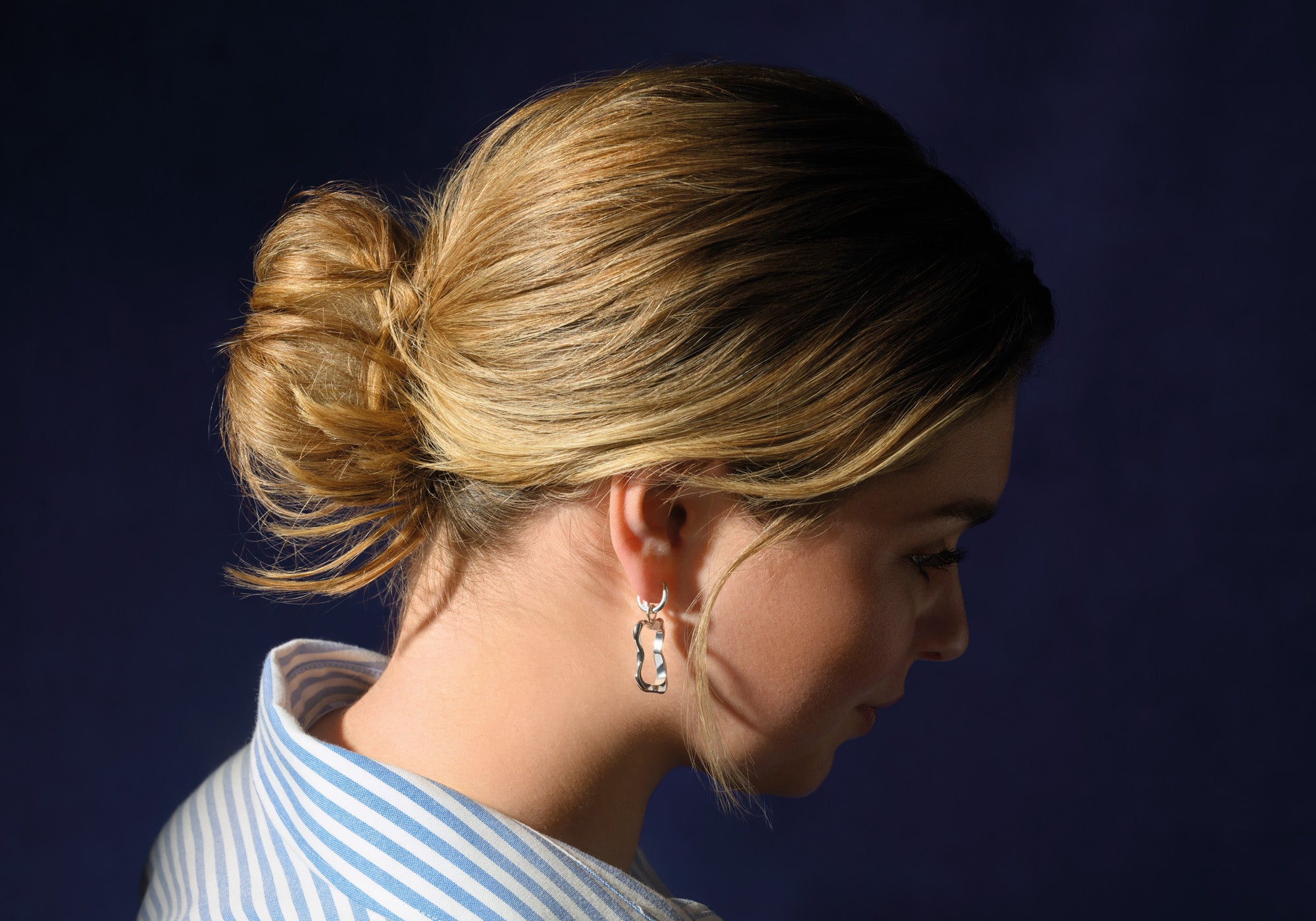 Model wearing handcrafted sterling silver earring drops in the shape of a pain au chocolat pastry.