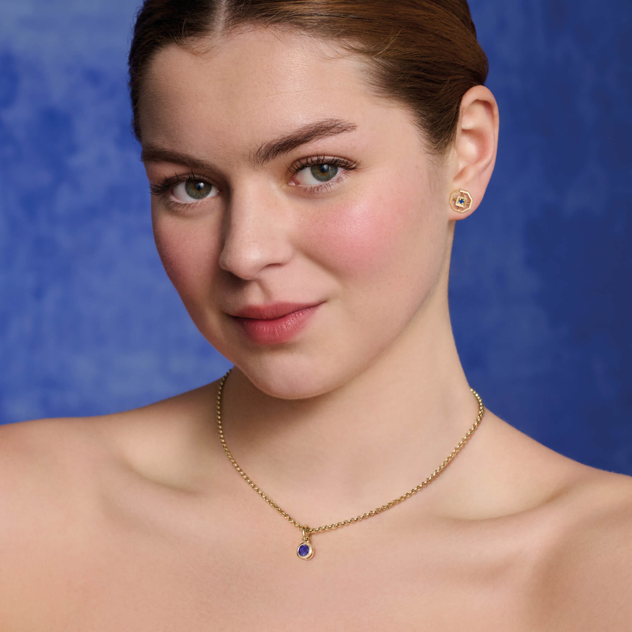 Model wearing handcrafted necklace pendant in yellow gold featuring a round blue precious stone drop