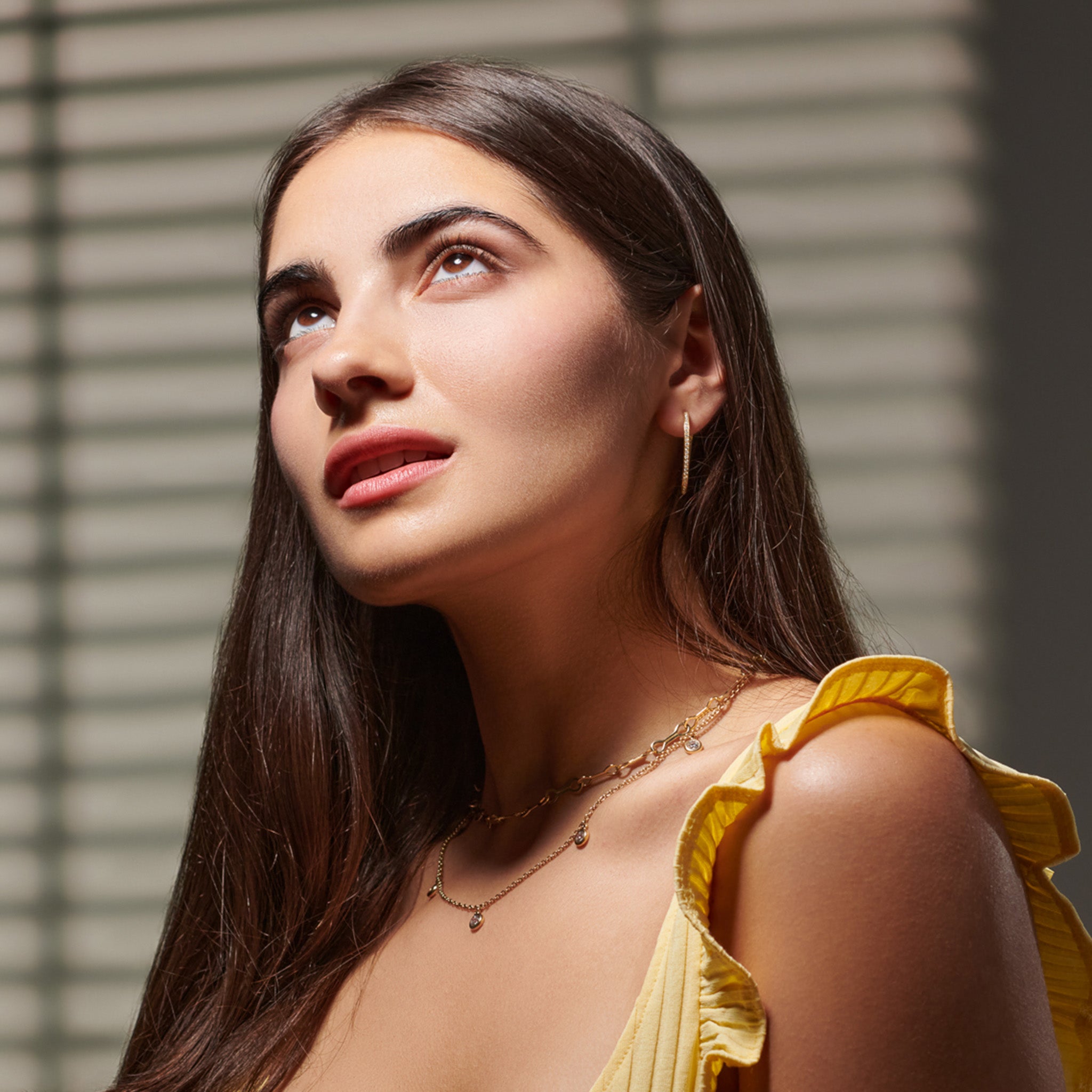 Model wearing a handcrafted necklace in precious metal with five round precious stone drops.