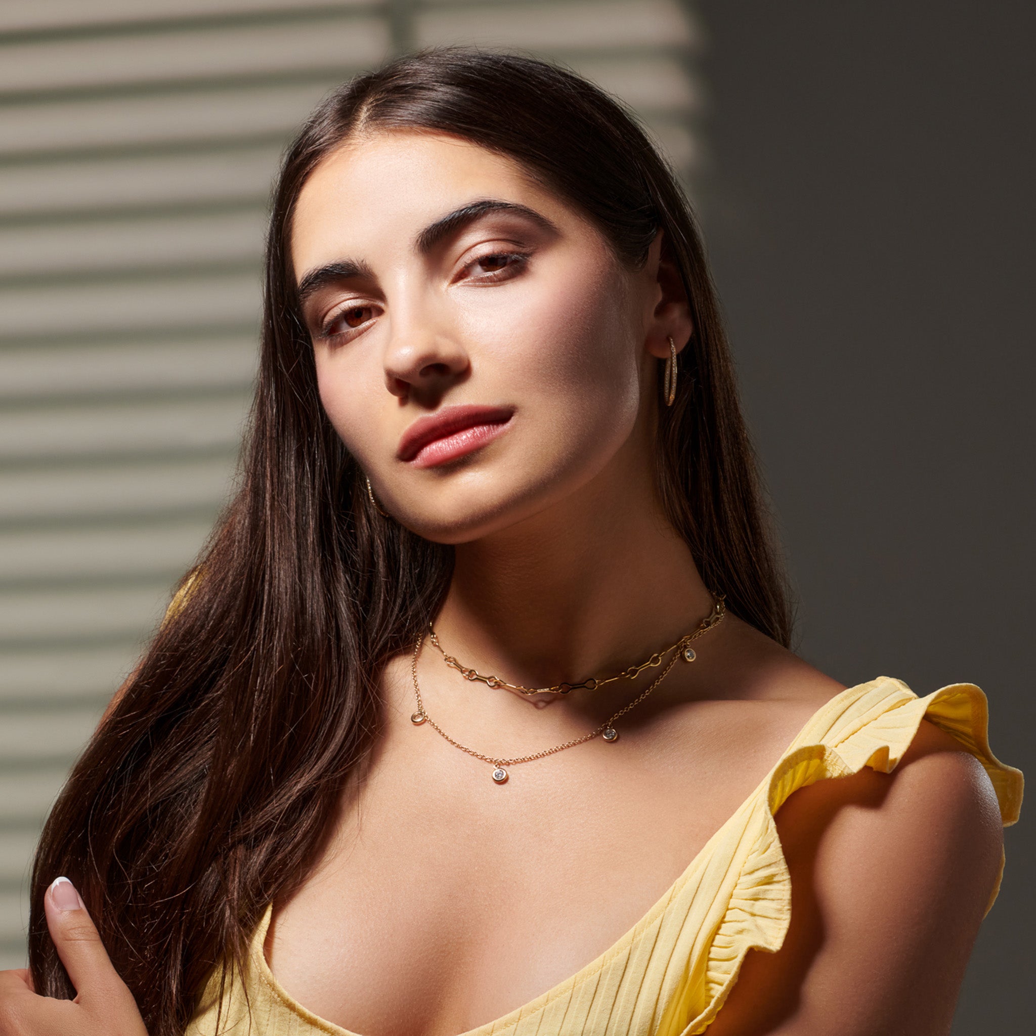 Model wearing a handcrafted necklace in precious metal with five round precious stone drops.