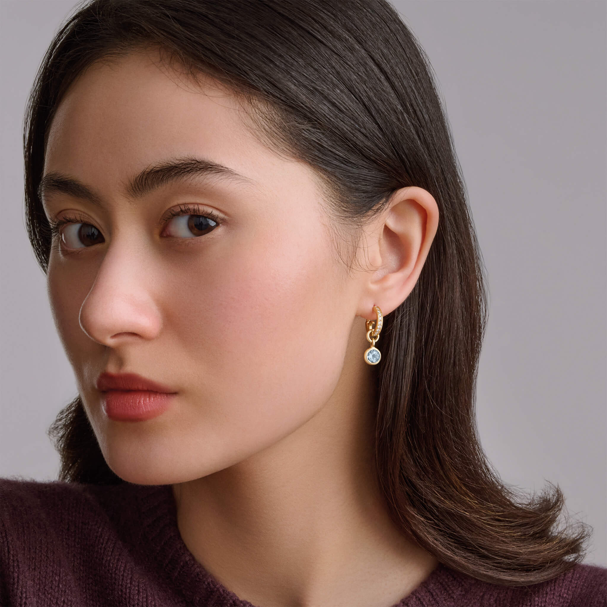 Model wearing handcrafted earring drops in precious metal with round precious stones.