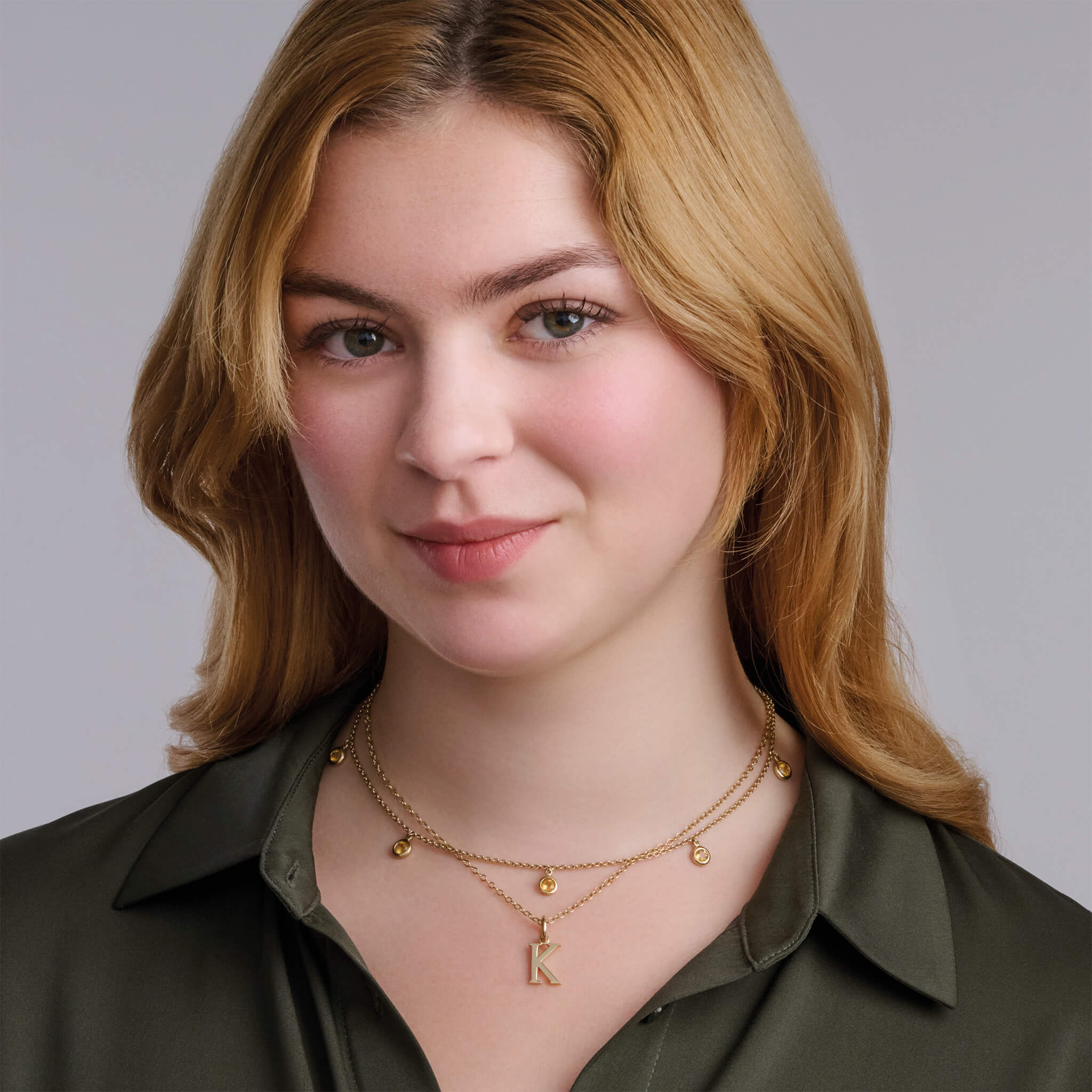 Model wearing a handcrafted necklace in precious metal with five round precious stone drops.