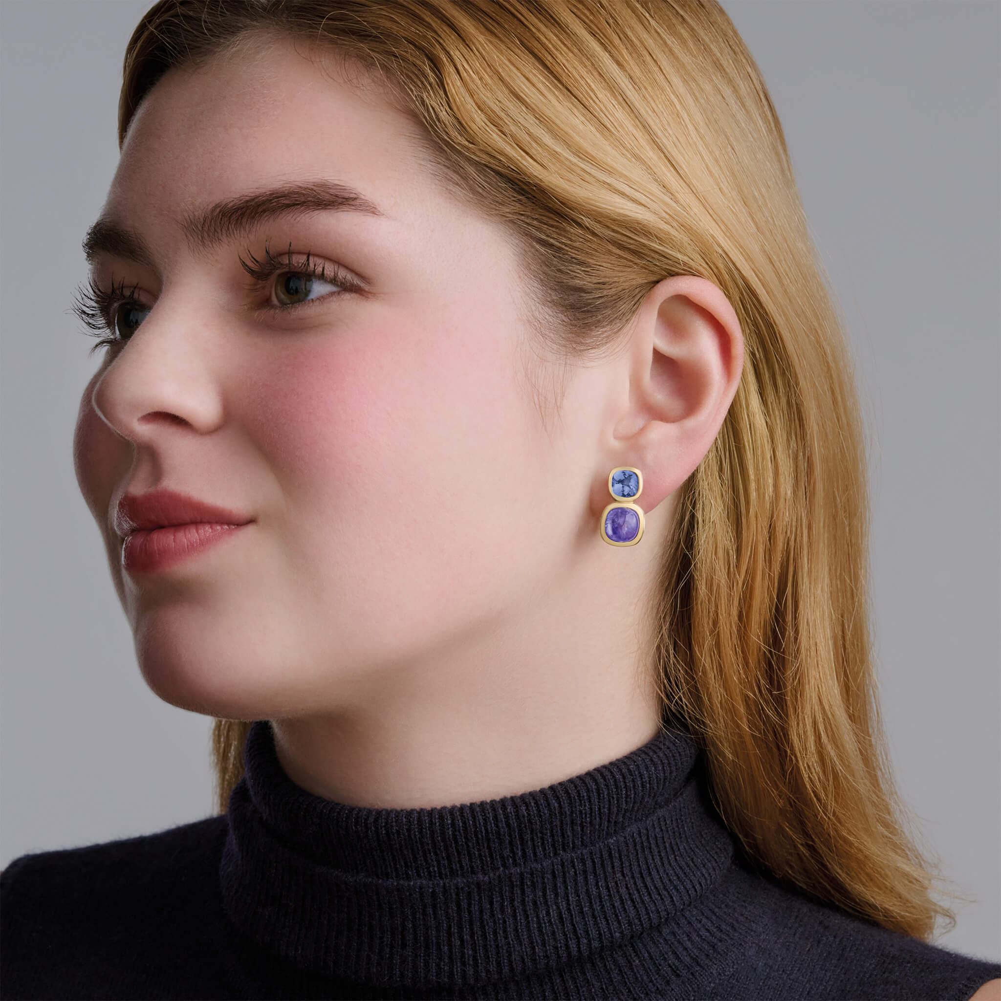 model wears handcrafted 18ct yellow gold square shaped earrings featuring precious gemstones.