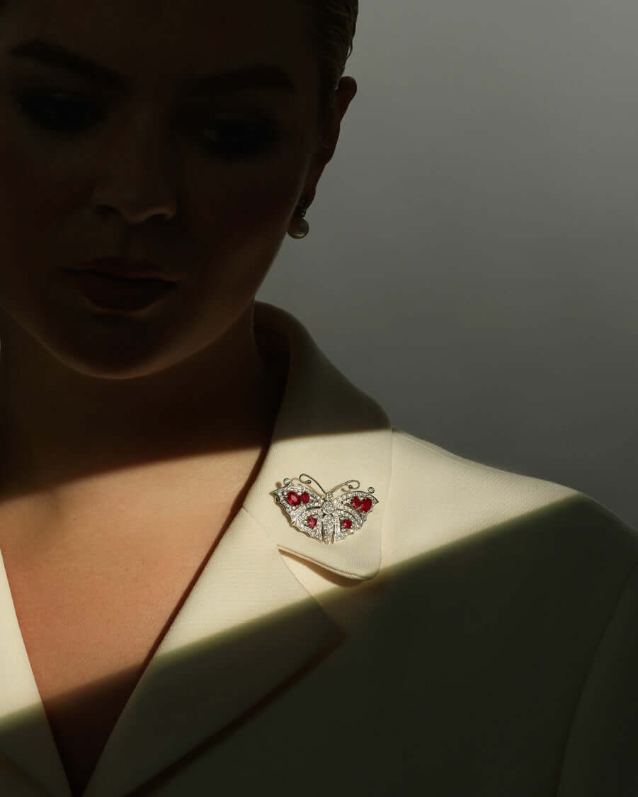 Model wearing a butterfly shaped pendant as a brooch in 18ct white gold with diamonds and rubies.