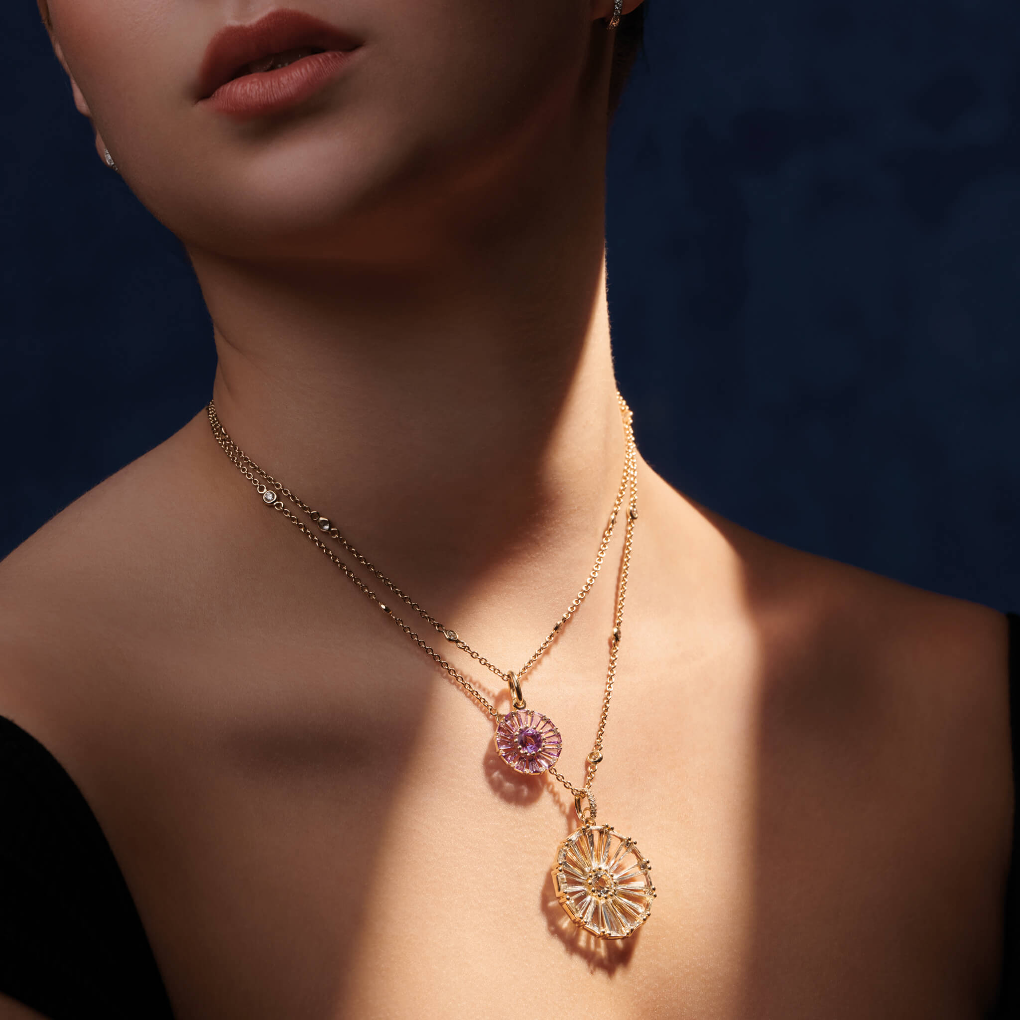 Model wearing a handcrafted yellow gold circular large necklace pendant with baguette cut white topaz and diamond gemstones.