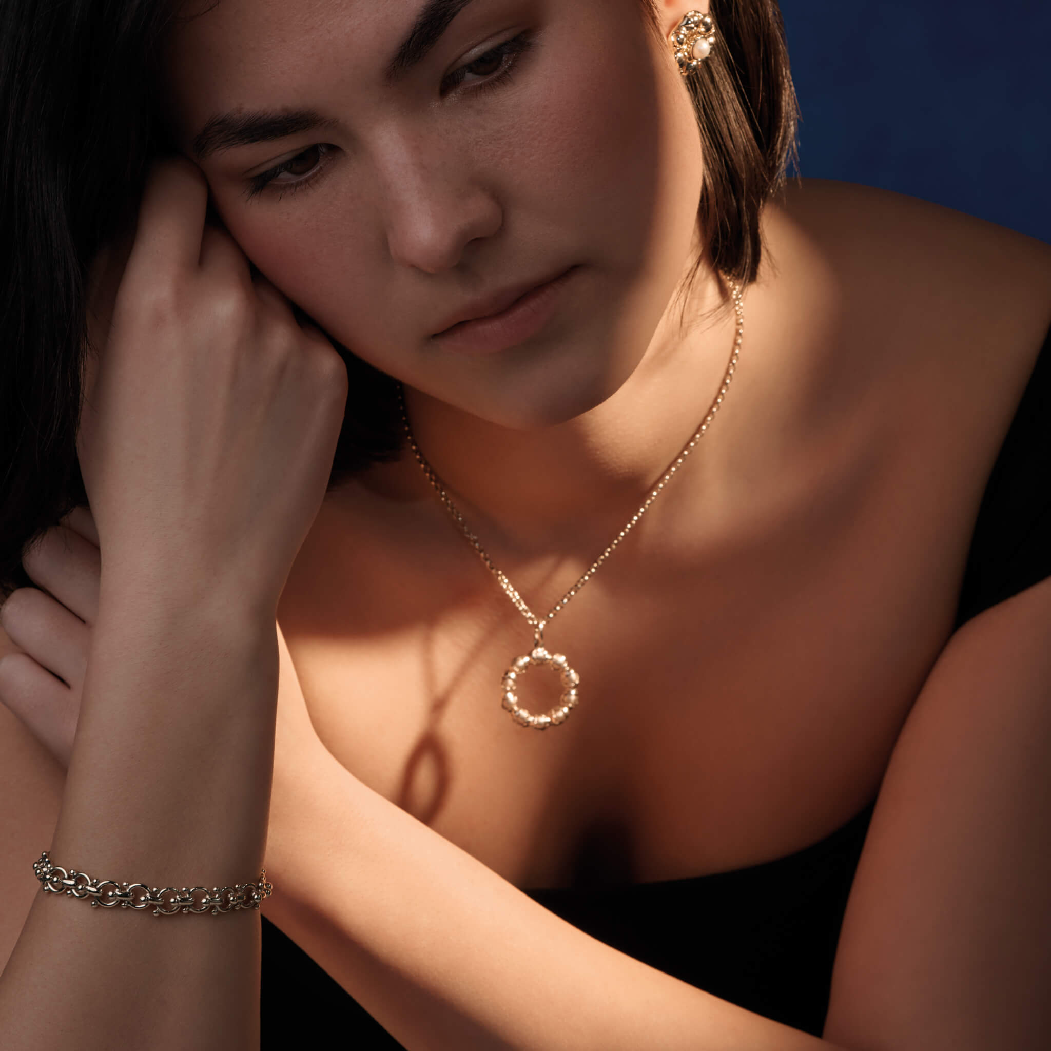 Model wearing a handcrafted precious metal necklace pendant featuring beads wrapped in leaves.
