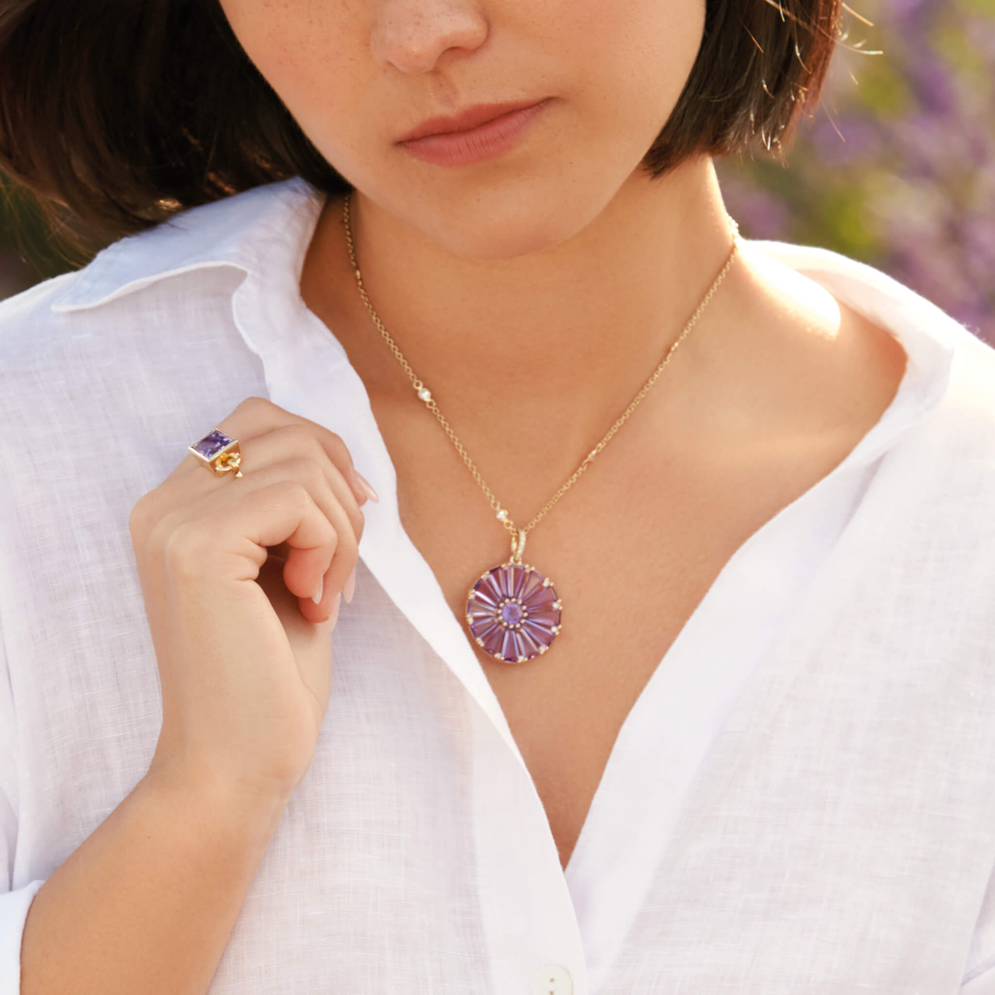 Model wearing a handcrafted yellow gold circular necklace pendant with baguette cut amethyst and diamond gemstones.