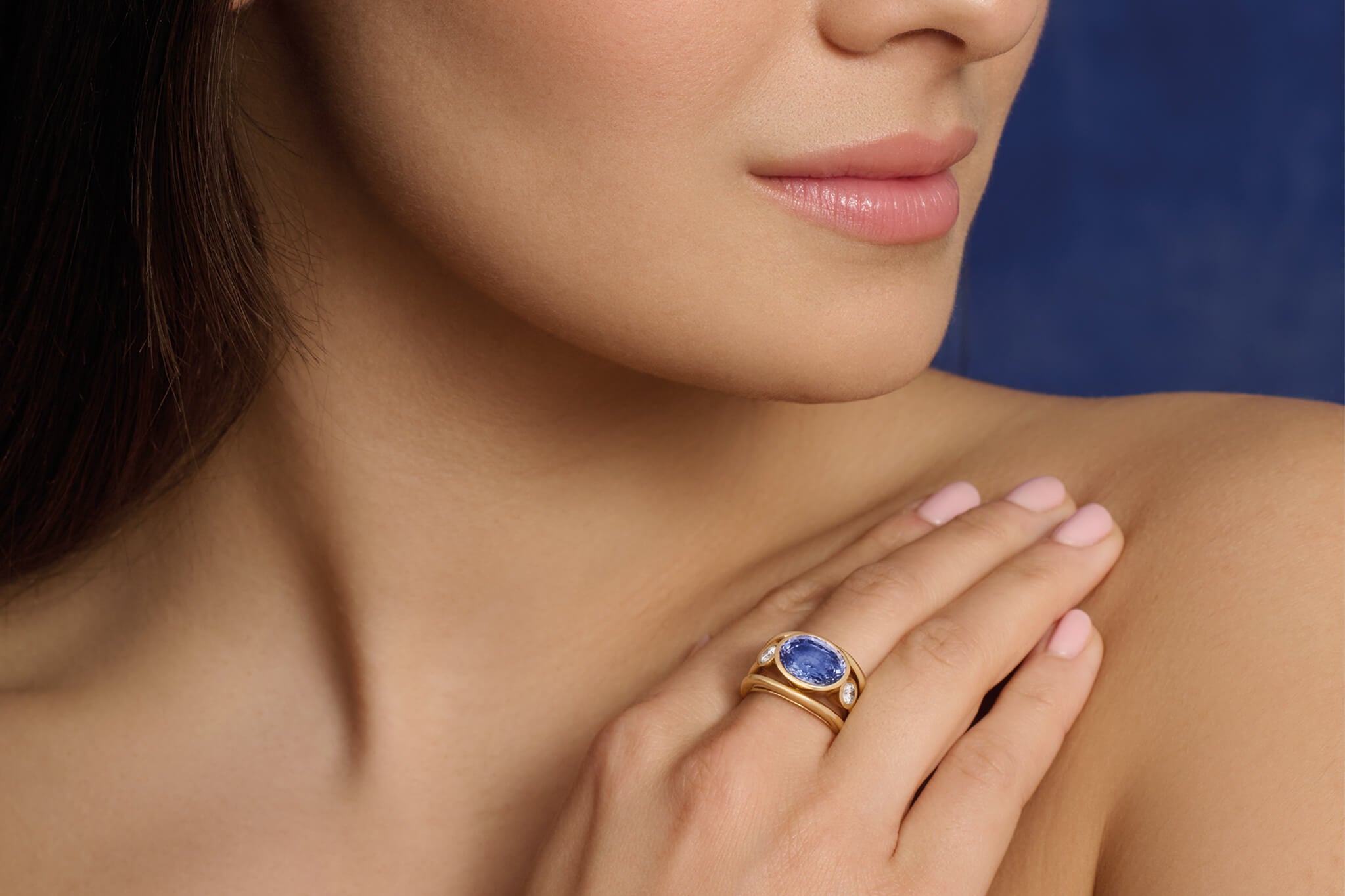 Model wearing sapphire Aeneus ring with diamonds set in yellow gold.