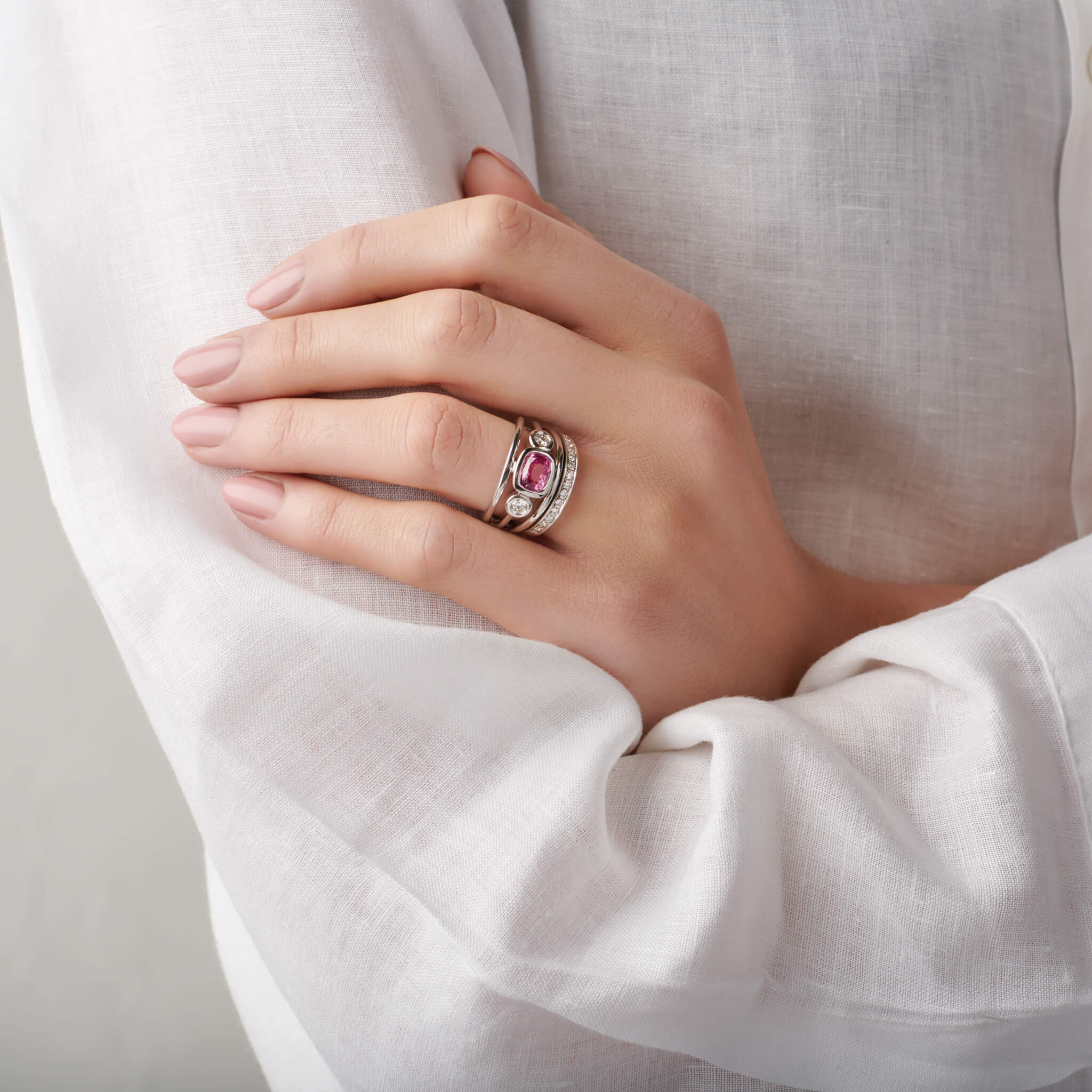 Model wears handcrafted 18ct white gold ring with an oval pink sapphire, the birthstone of September, flanked by two round diamonds.