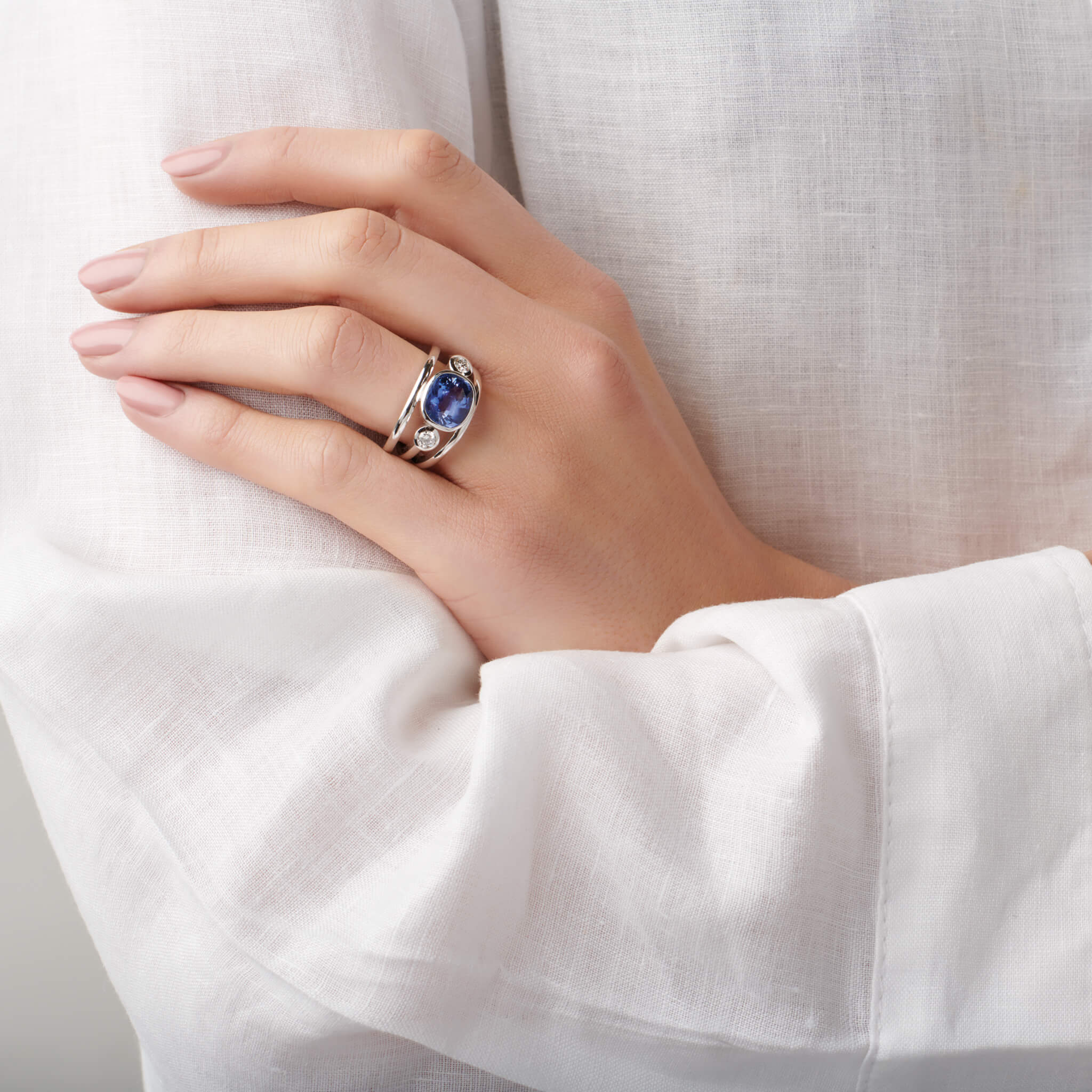 Model wears handcrafted 18ct white gold ring with an oval sapphire, the birthstone of September, flanked by two round diamonds.