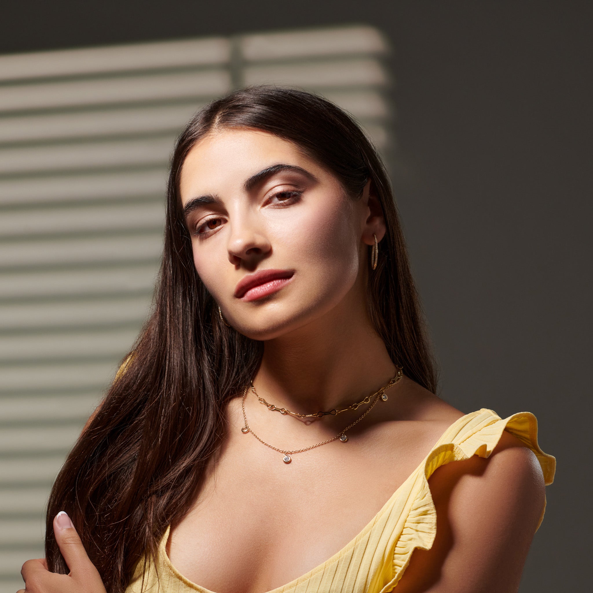 Model wearing a handcrafted necklace in precious metal with five round precious stone drops.