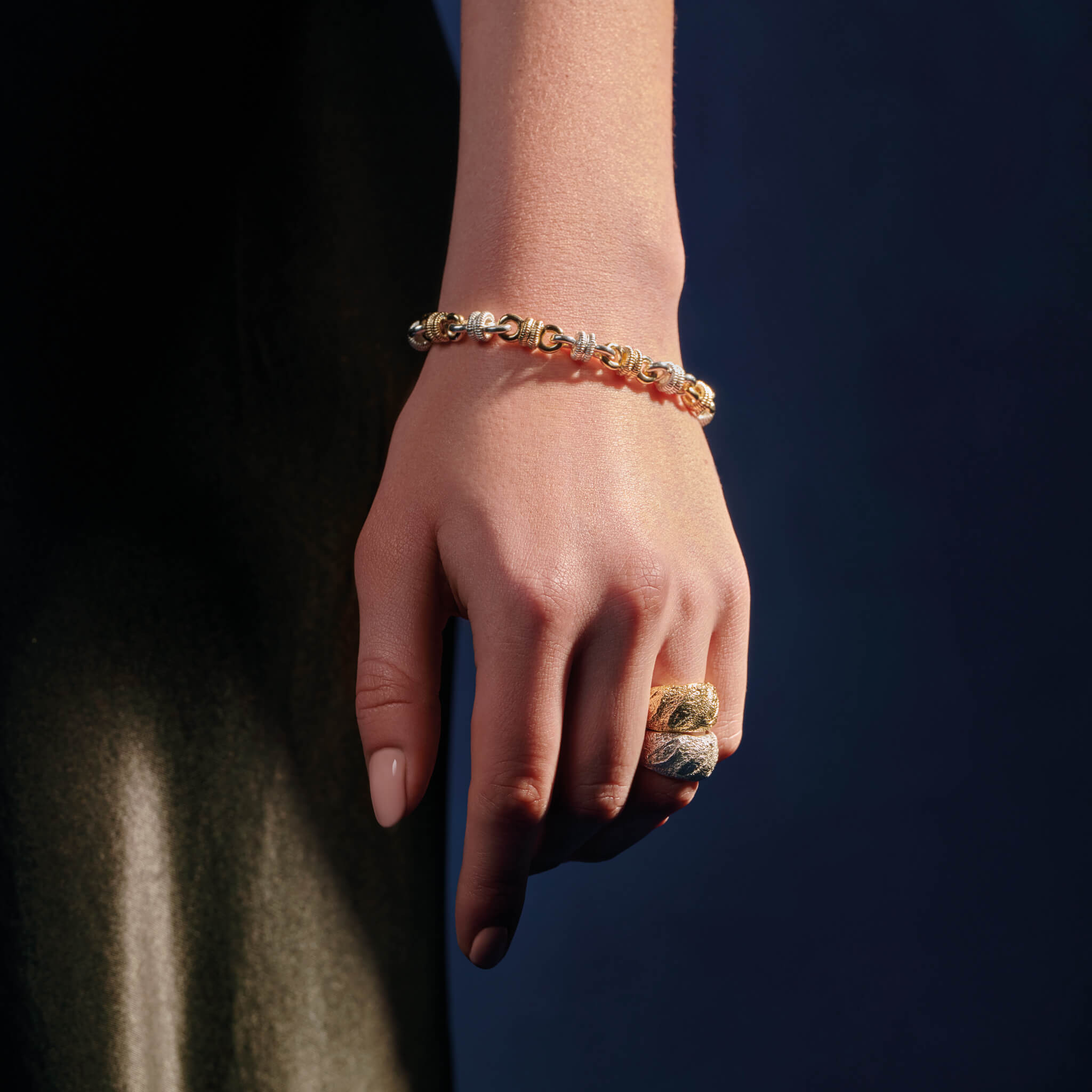 Model wearing a handcrafted yellow gold and sterling silver bracelet featuring alternating textured metal links.