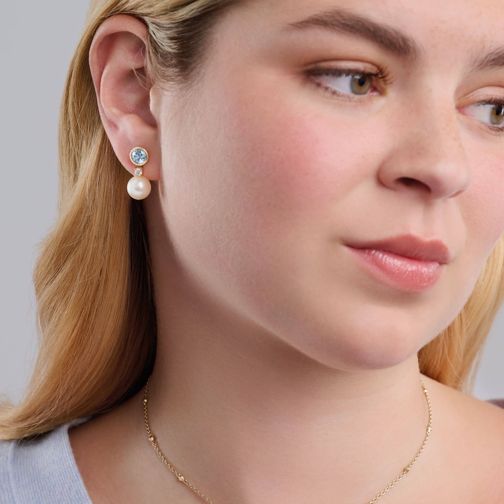 Model wearing handcrafted yellow gold halo earring drops with a pearl and diamond.