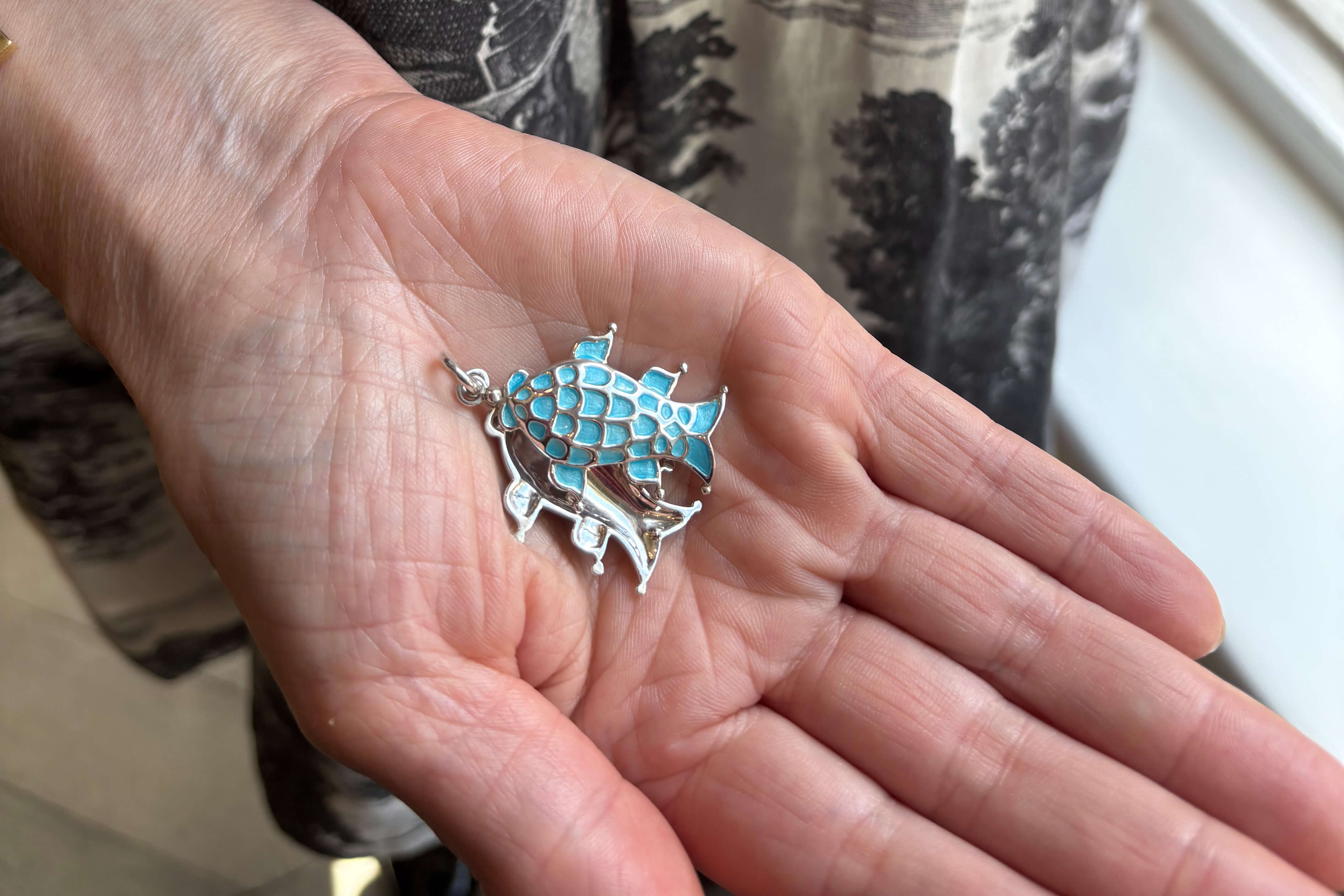 Cassandra hols a fish shaped charm which can open to reveal a polished silver surface perfect for engraving.