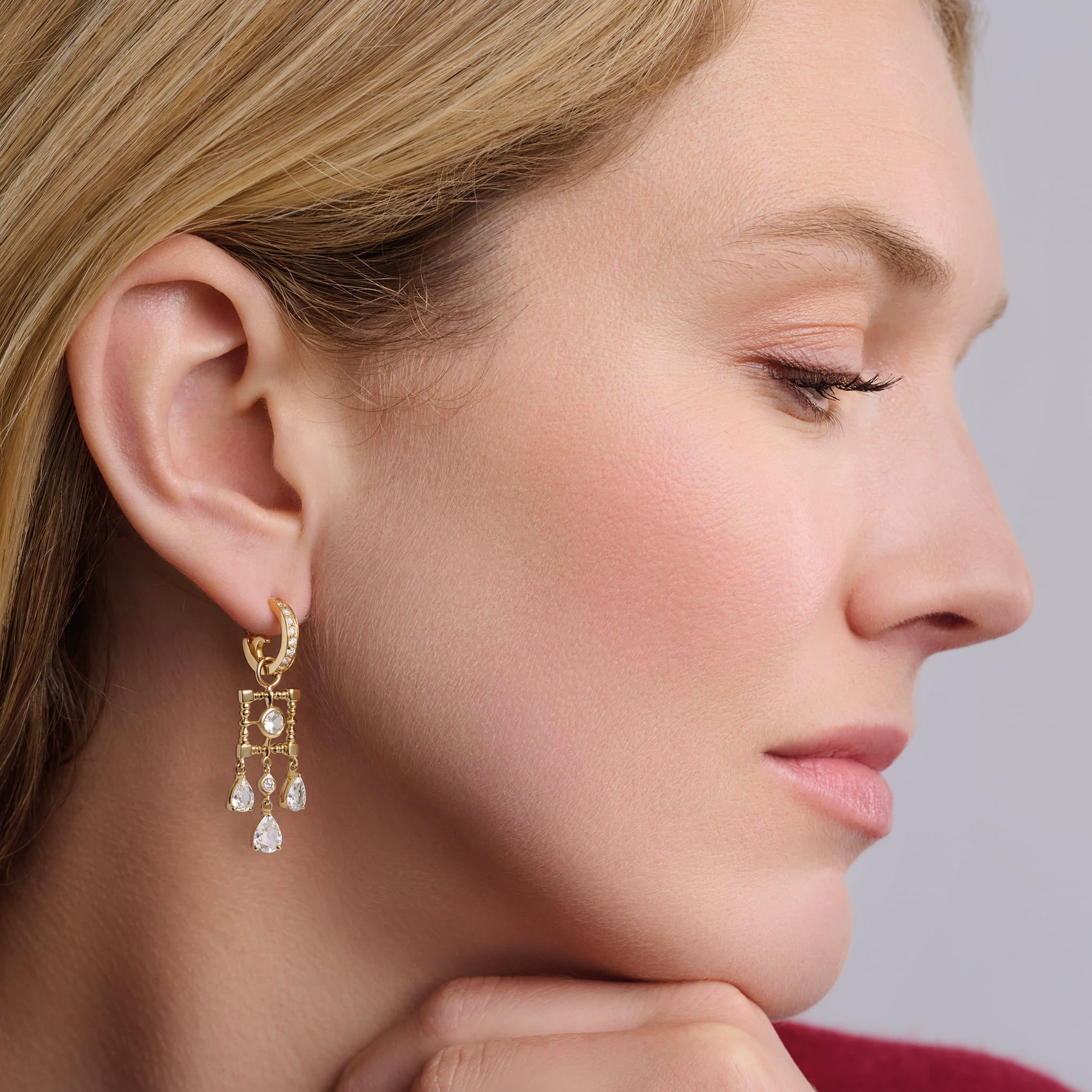 Model wearing handcrafted earring drops in precious metal featuring a teardrop-shaped design with precious stones.