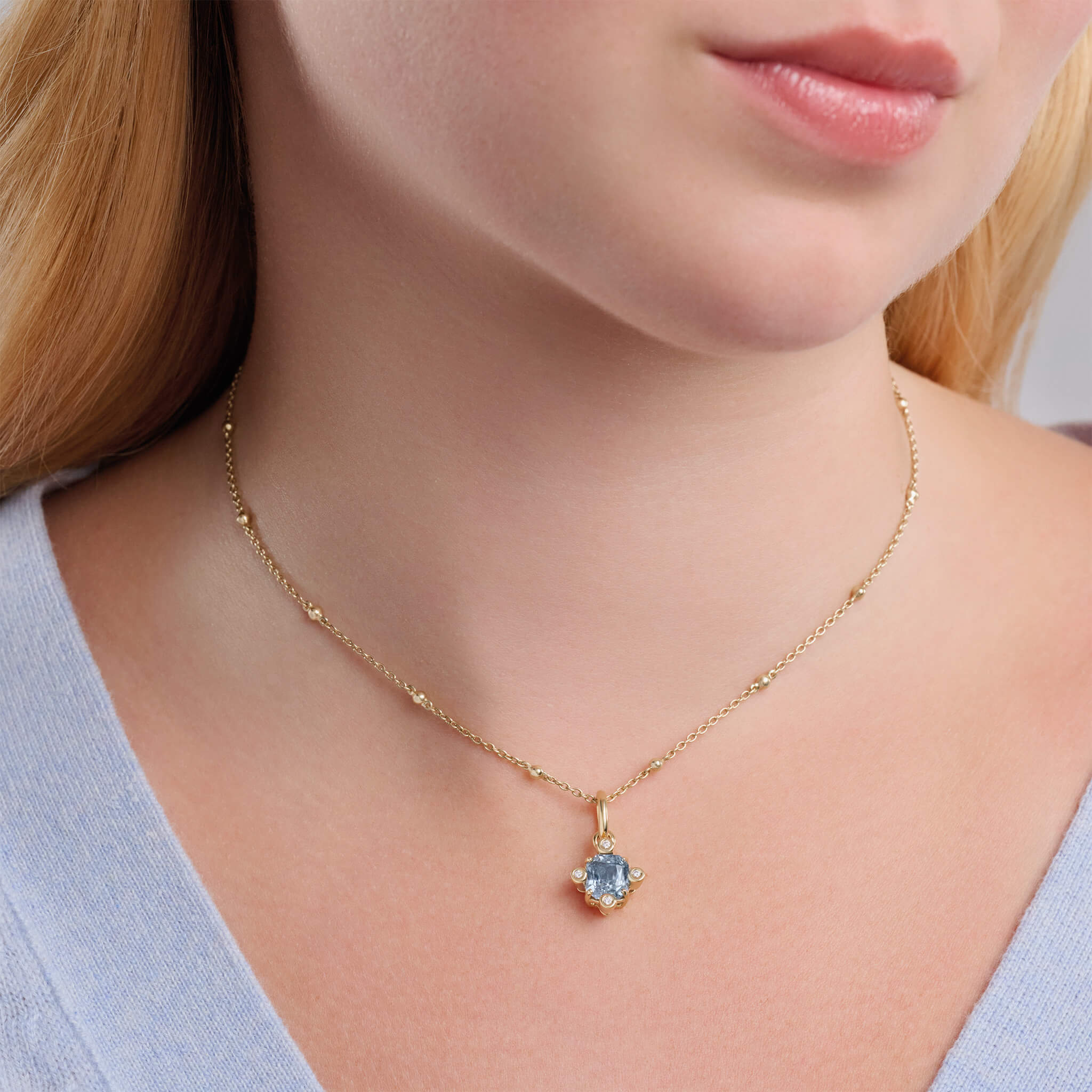 Model wearing handcrafted 18ct yellow gold Compass pendant with emerald-cut blue sapphire set with four diamonds, september birthstone