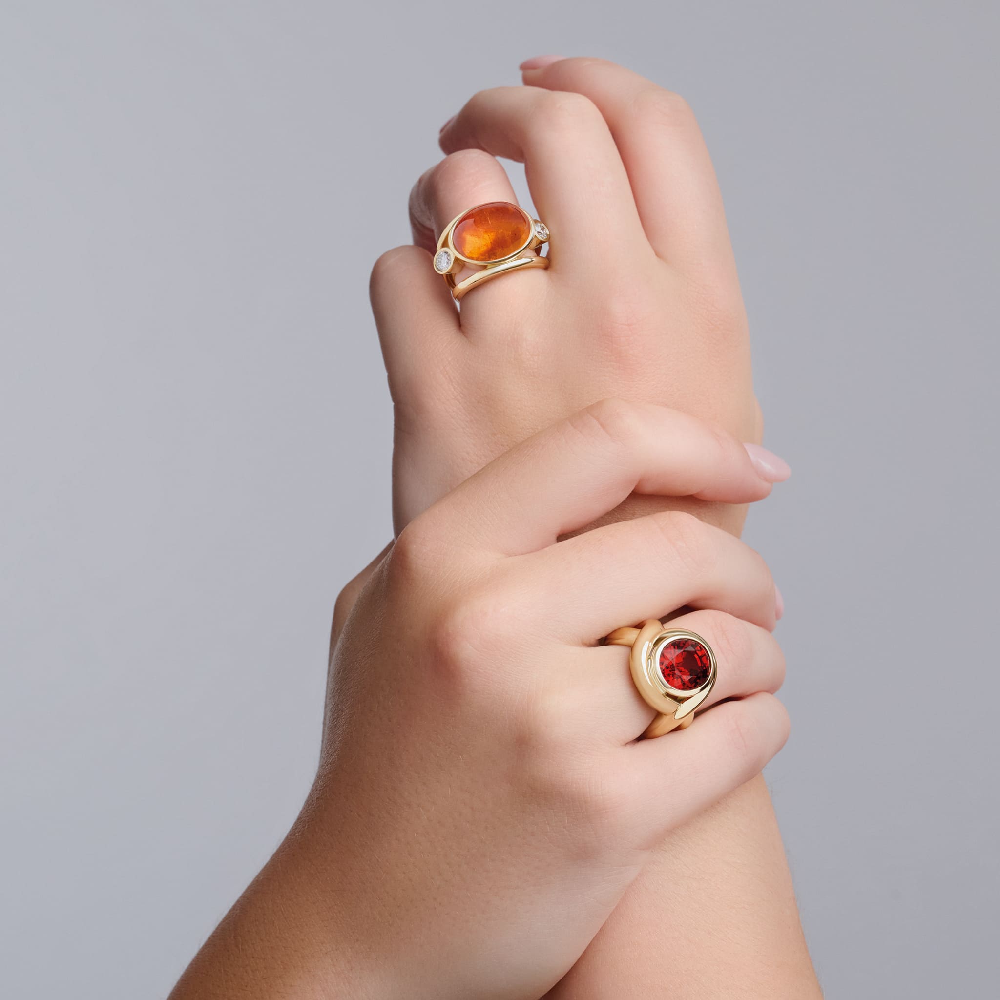 Model wearing handcrafted yellow gold ring featuring curved shanks with a unique spessartine garnet