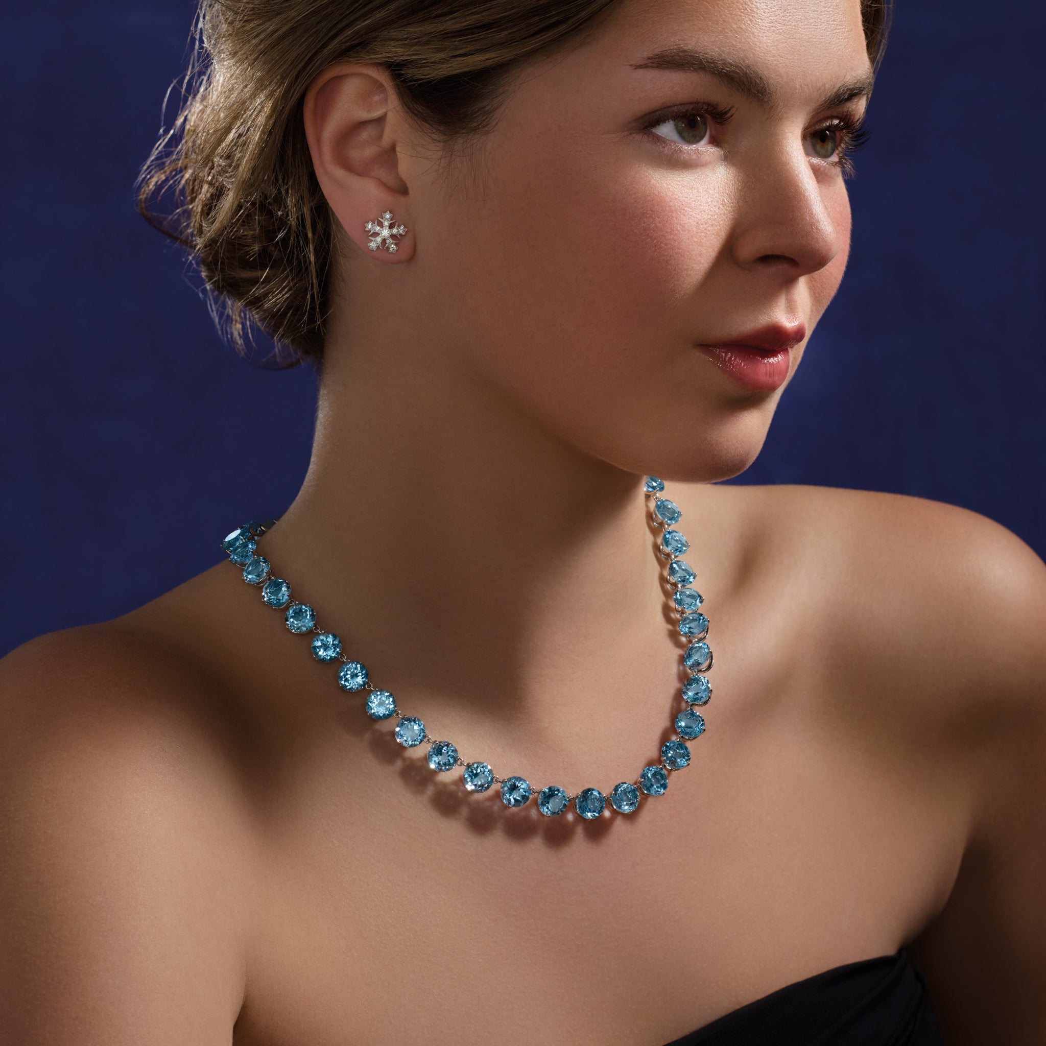Model wearing a handcrafted white gold necklace featuring circular blue topaz gemstones, november birthstone
