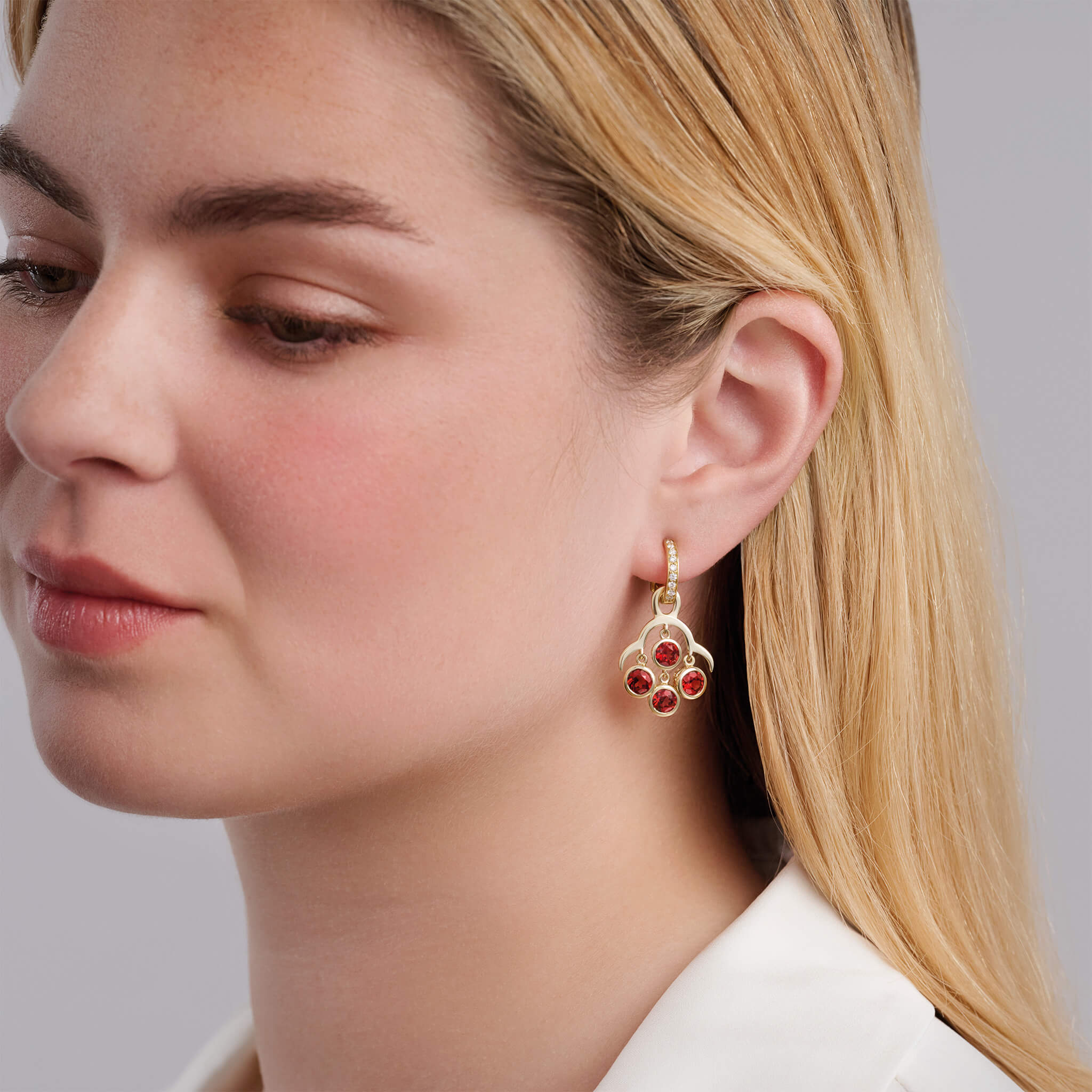Model wearing handcrafted yellow gold earring drops inspired by acai berries featuring four garnet gemstones