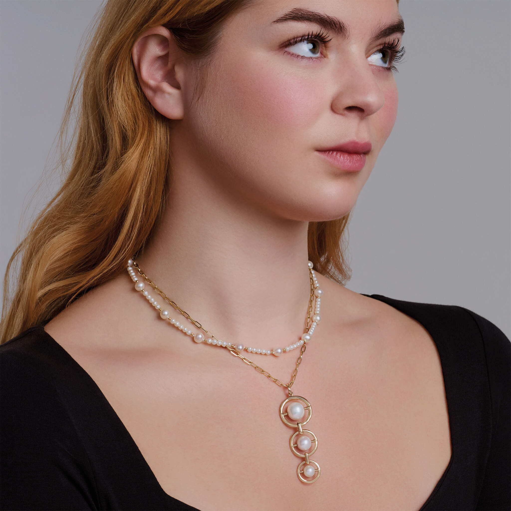 Model wears handcrafted yellow gold necklace pendant with three vertically aligned circular frames, each encircling a precious gemstone
