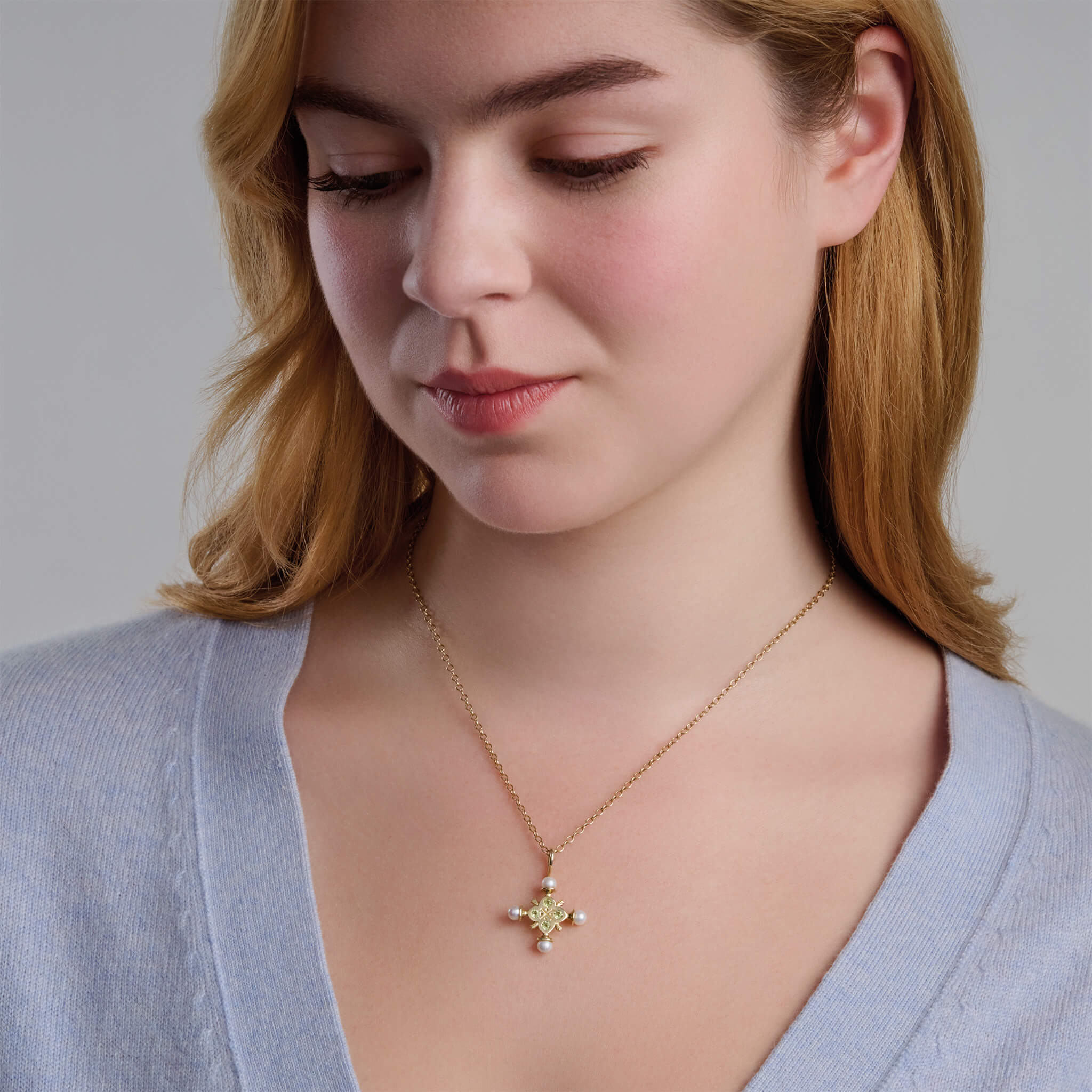 Model wearing handcrafted yellow gold cross pendant precious birthstone gem and pearl.