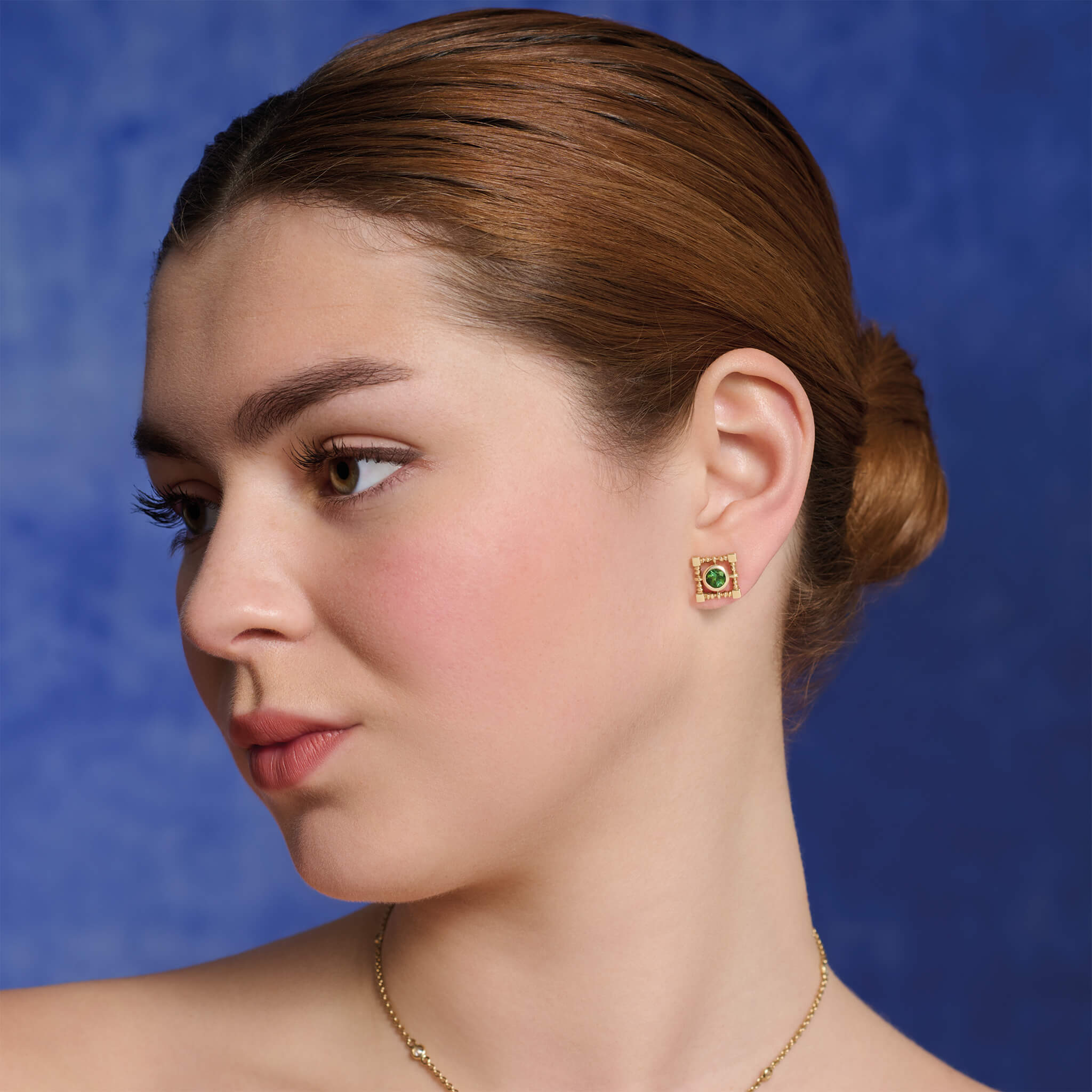 Model wears handcrafted yellow gold stud earrings in a square lattice shape with a central precious gemstone