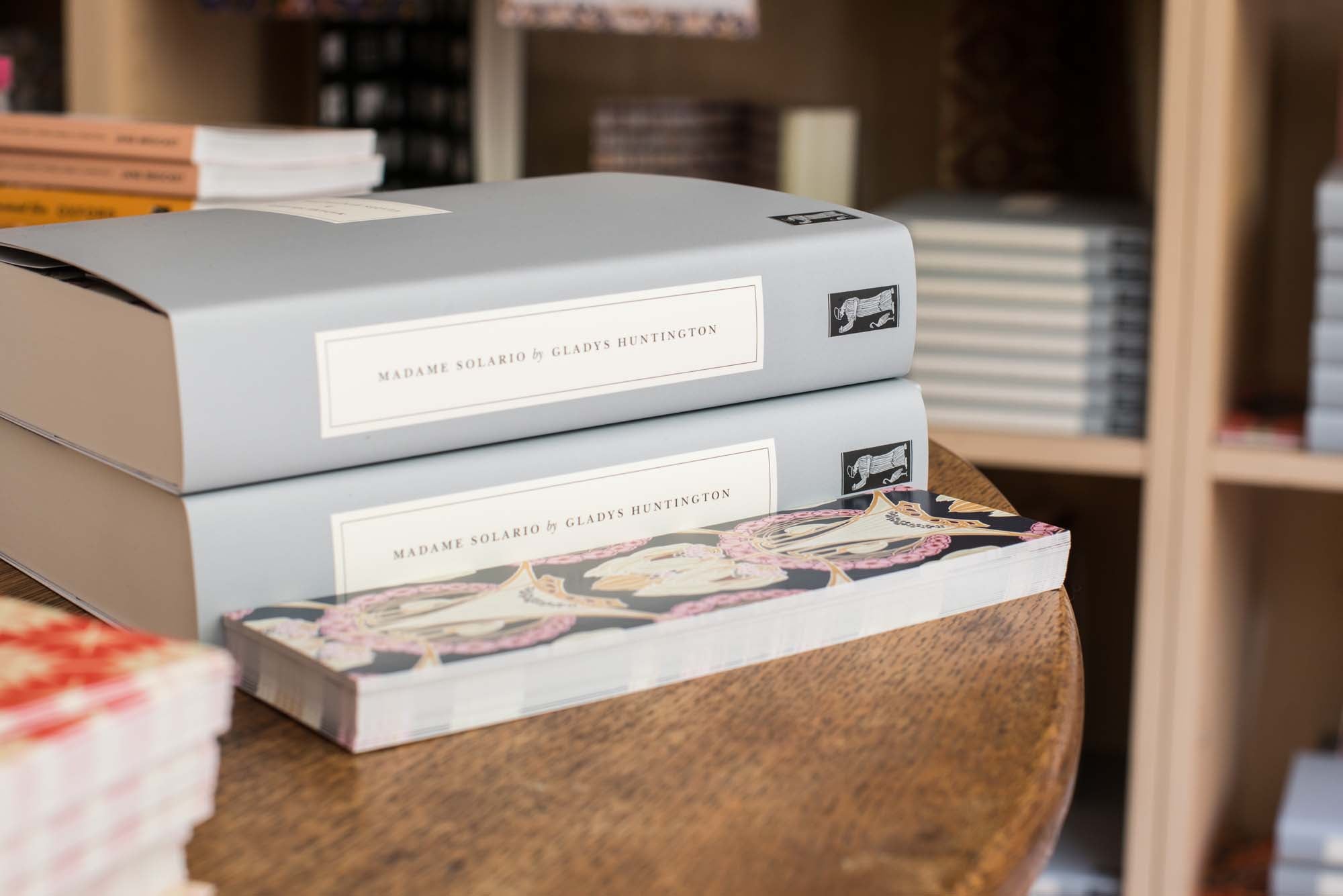 Two Persephone Books with their classic grey cover on wood table display in their bookstore. 